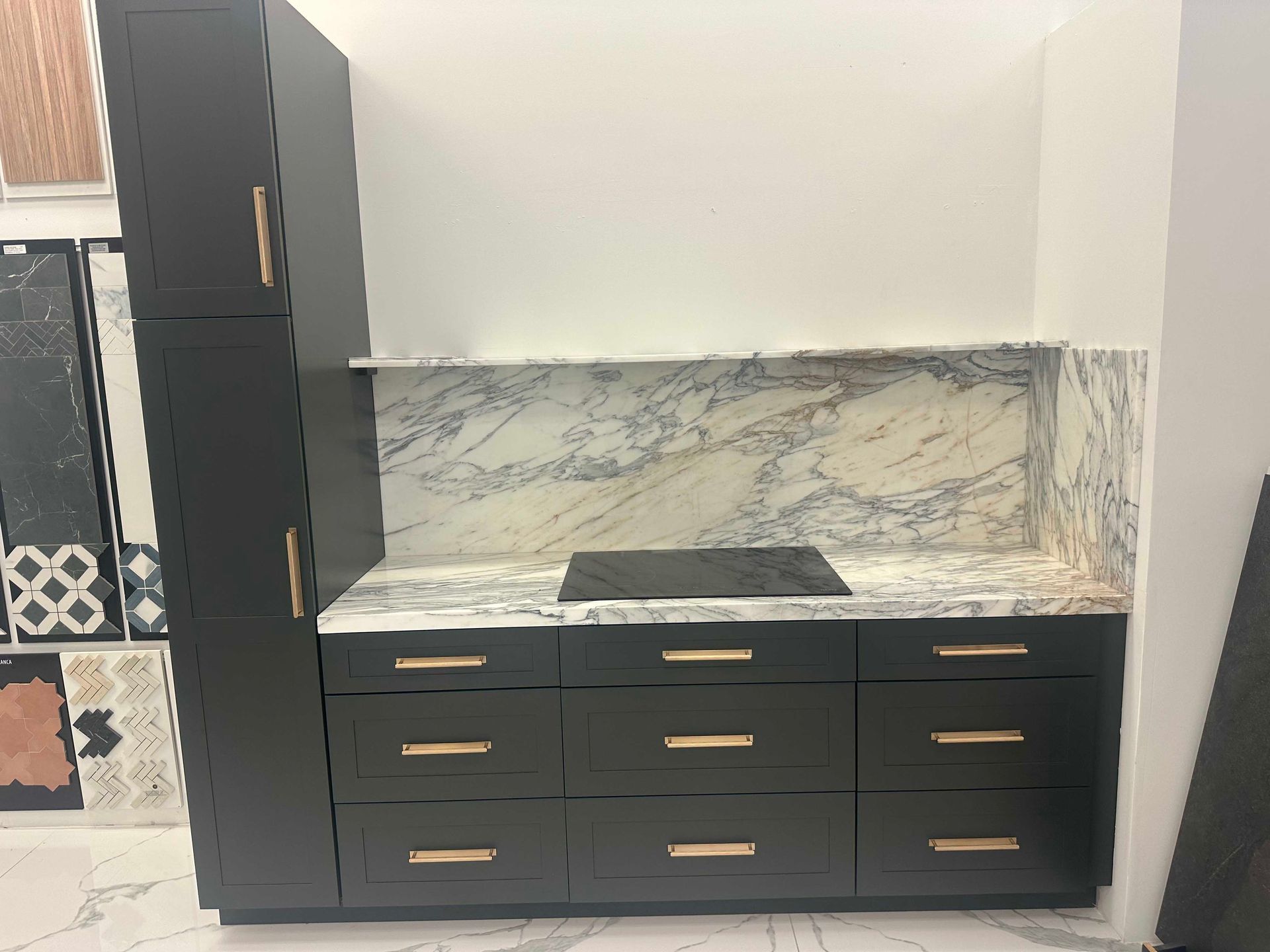 Dark gray kitchen cabinets with copper hardware, marble backsplash, and built-in stovetop.