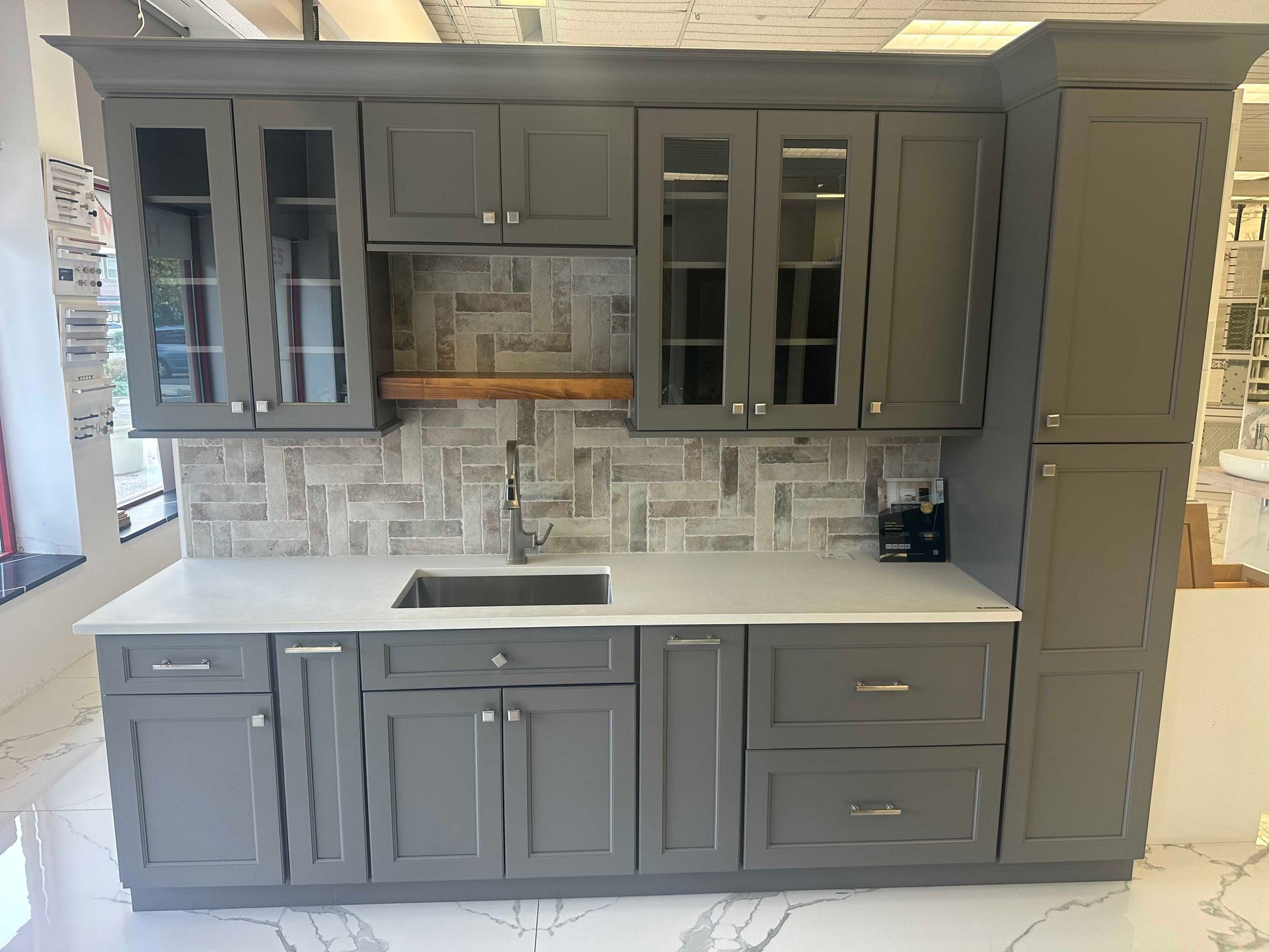 Gray kitchen cabinets with a white countertop and tile backsplash.