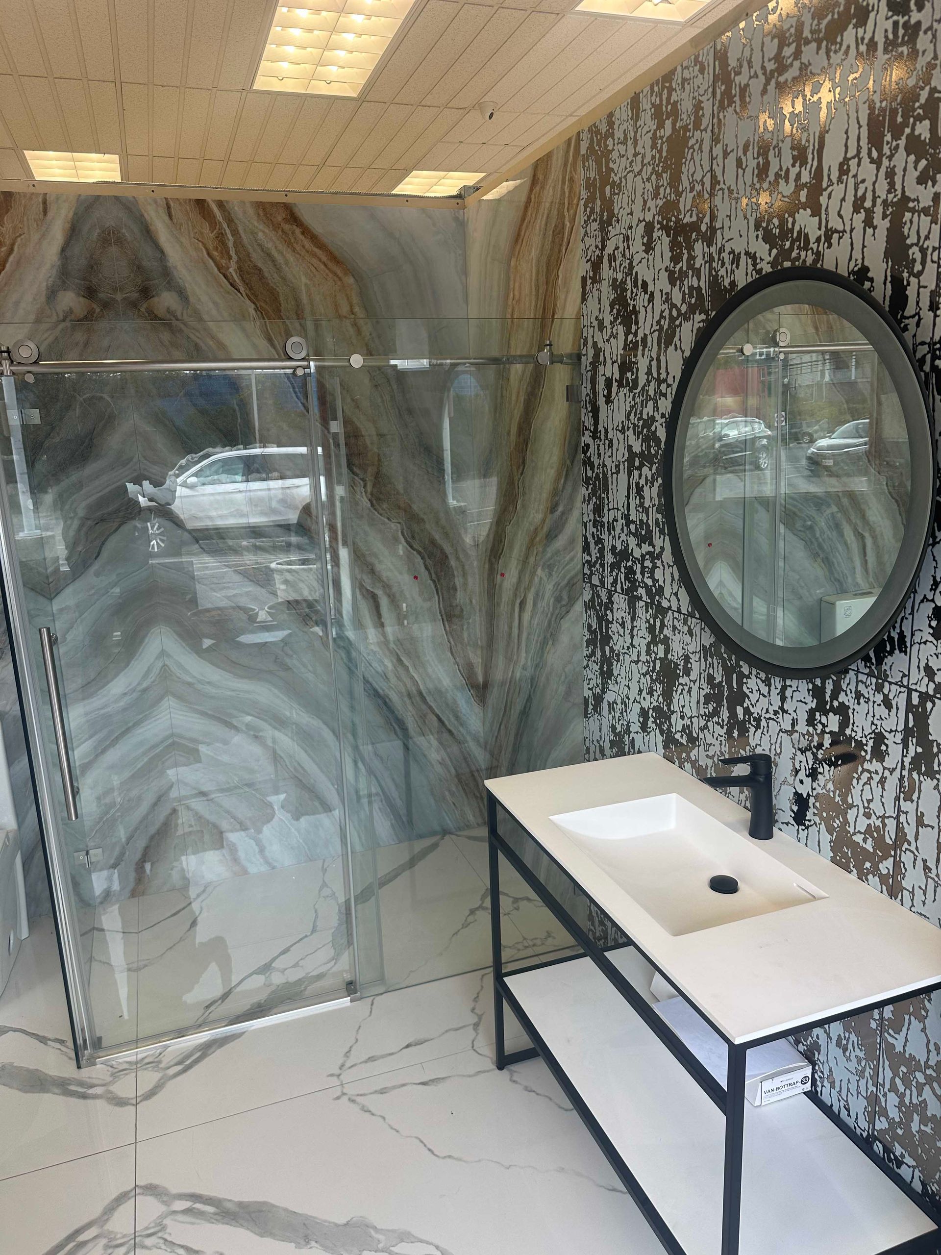 Bathroom with abstract patterned tile, glass shower, black fixtures, and a round mirror.