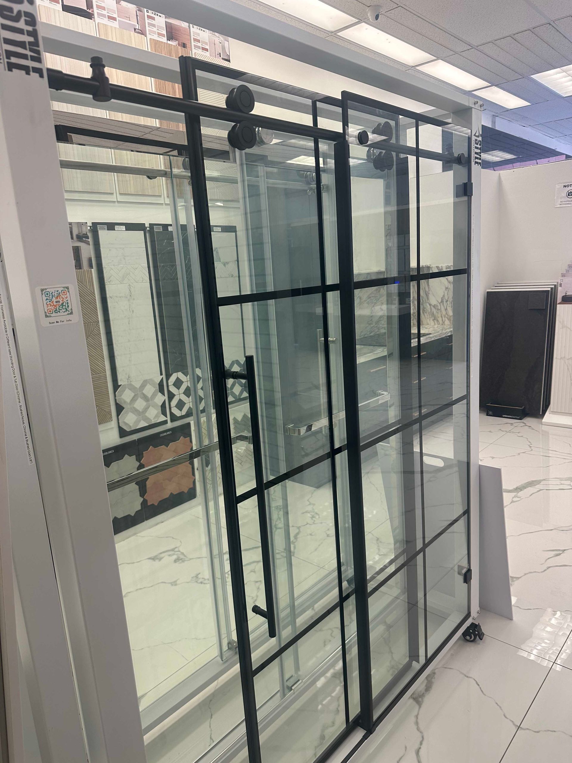 Sliding glass door with black metal frame and handle. In a showroom, with other displays visible.