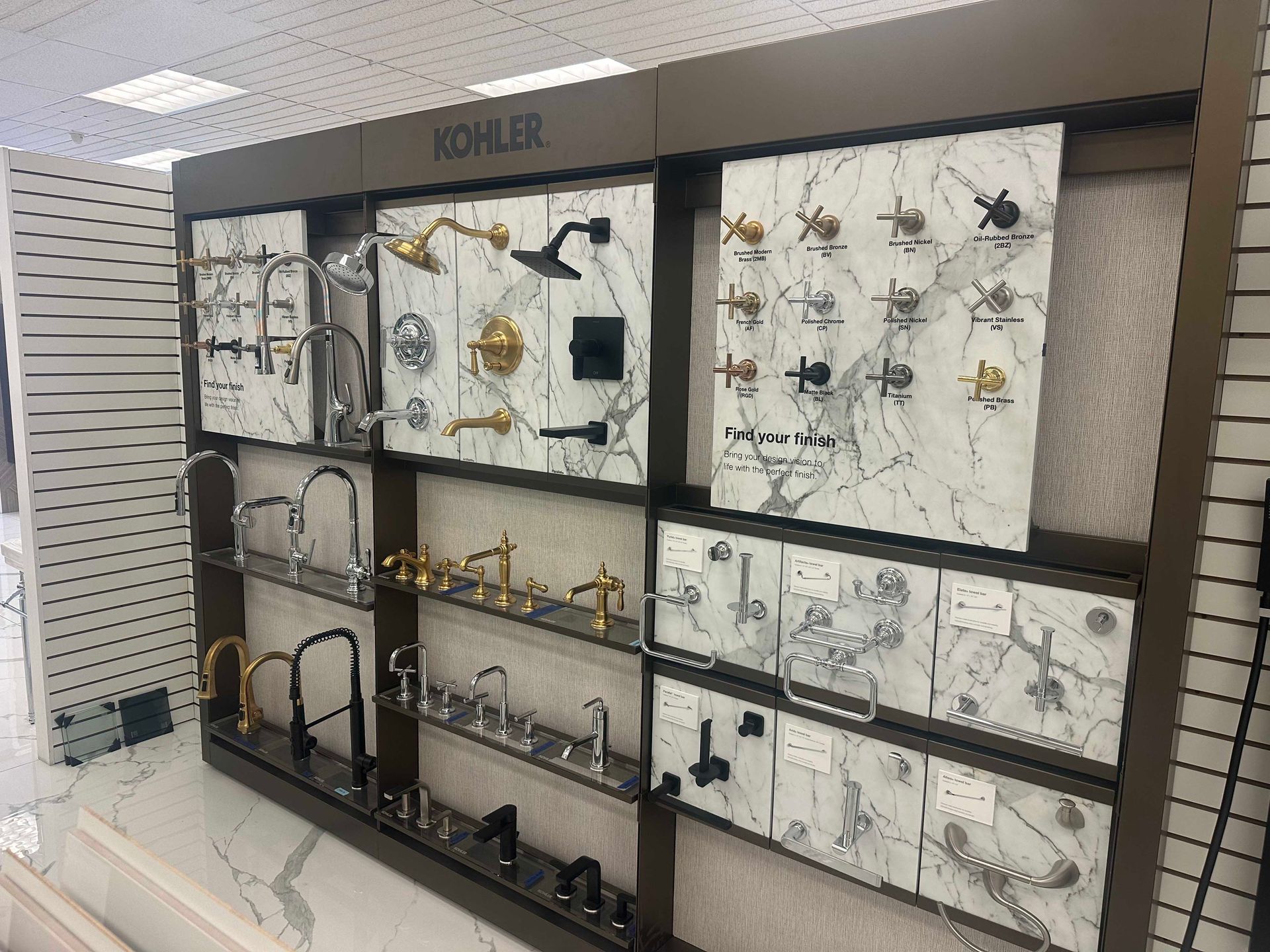 KOHLER bathroom fixtures display in a showroom, various styles and finishes, mounted on marble-look panels.