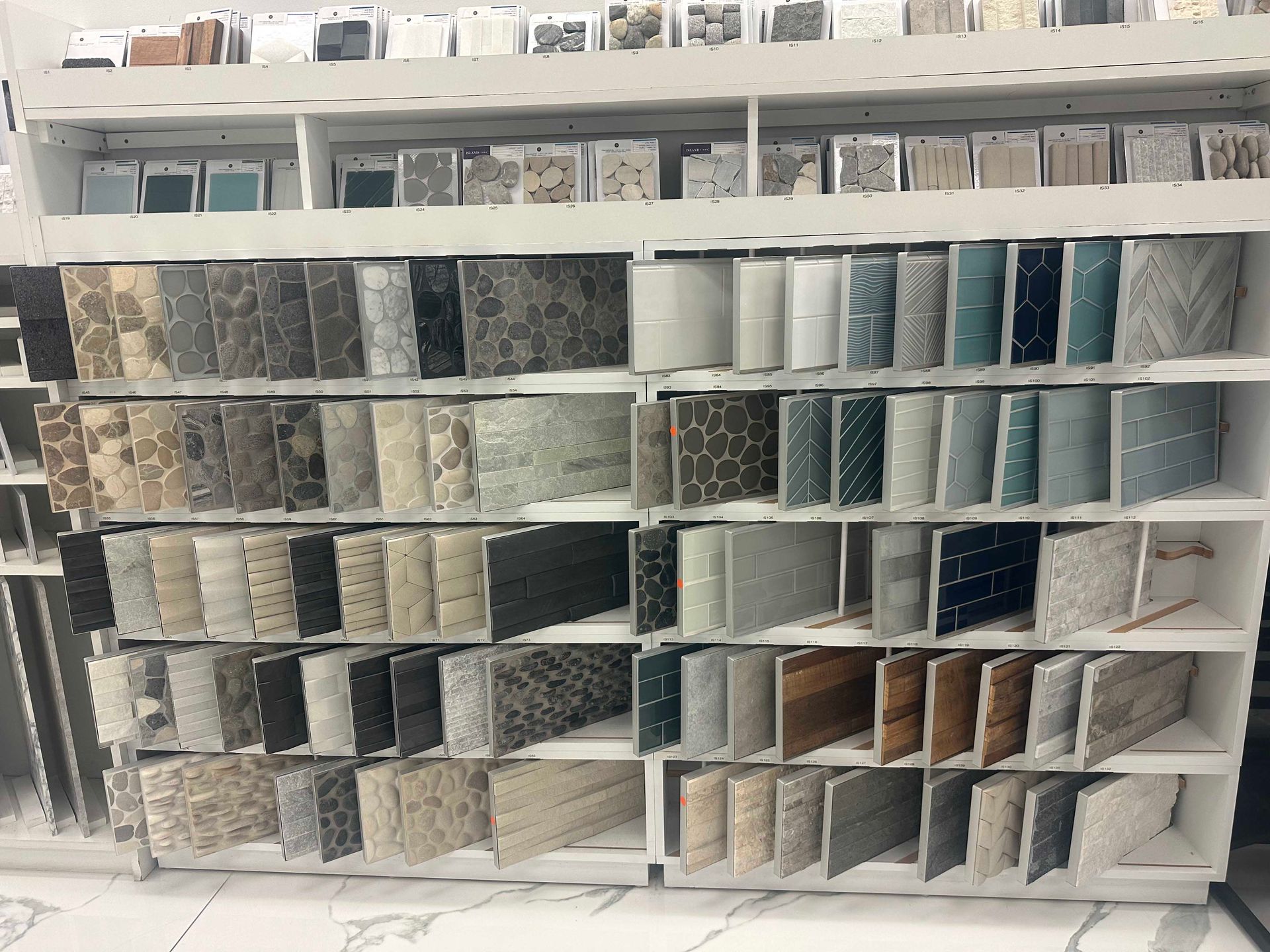 Shelves displaying numerous tile samples, varying colors, textures, and patterns in a showroom setting.