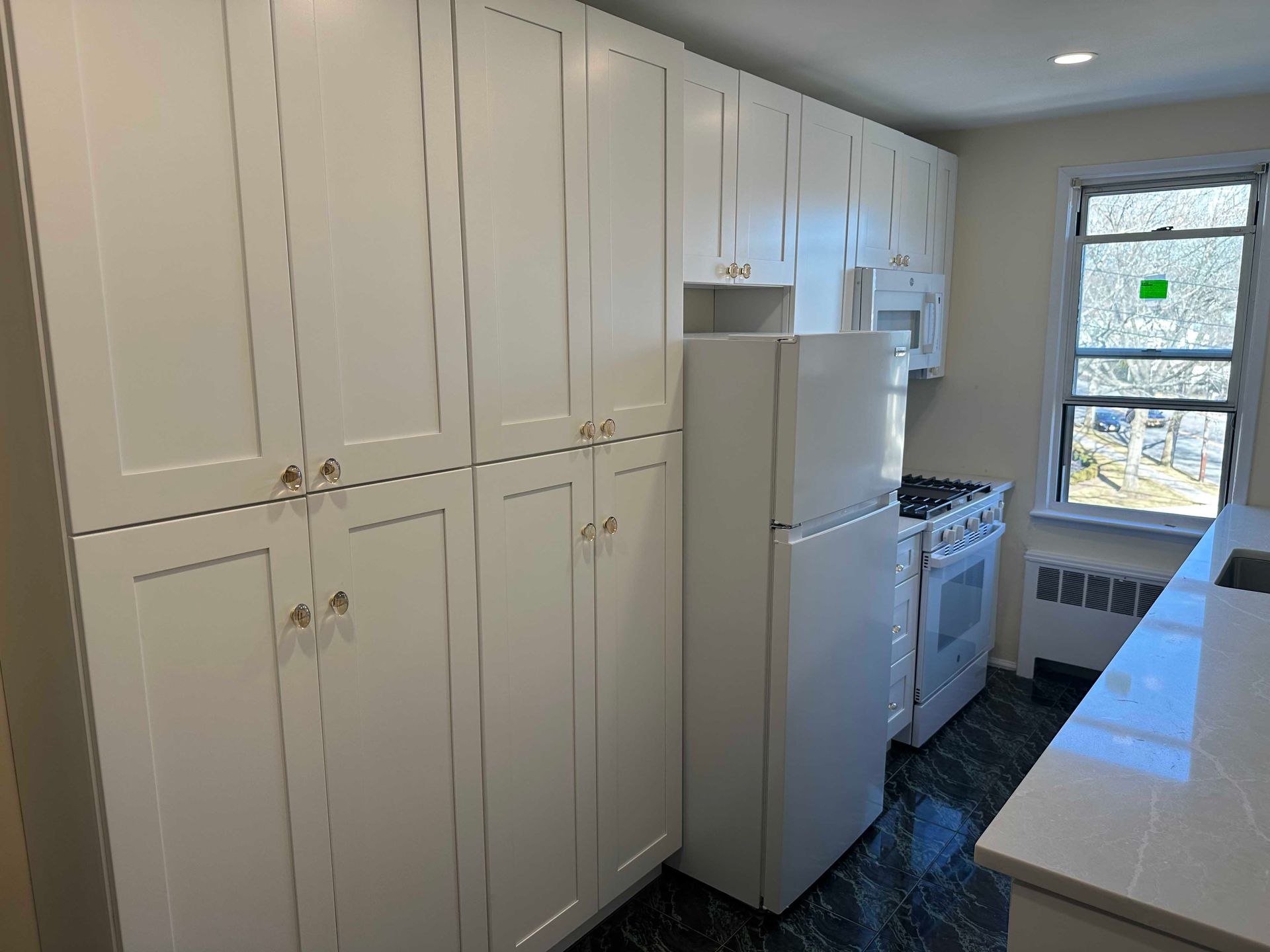 White kitchen cabinets and appliances in a room with a window.