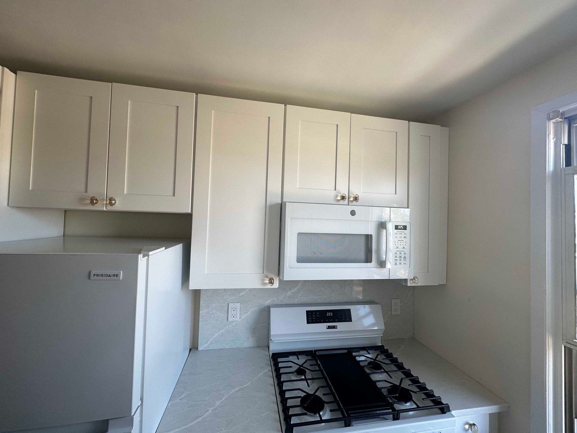 White kitchen cabinets above a gas stove and microwave. Refrigerator visible on left.