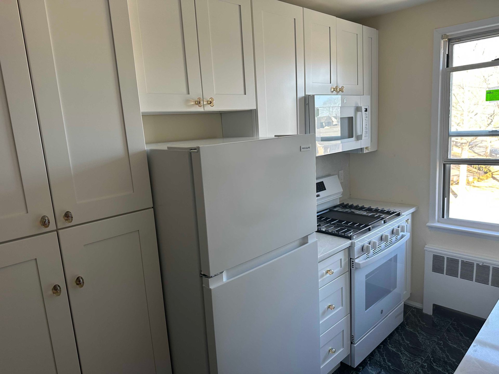 White kitchen with cabinets, refrigerator, stove, and microwave. Window to the right.