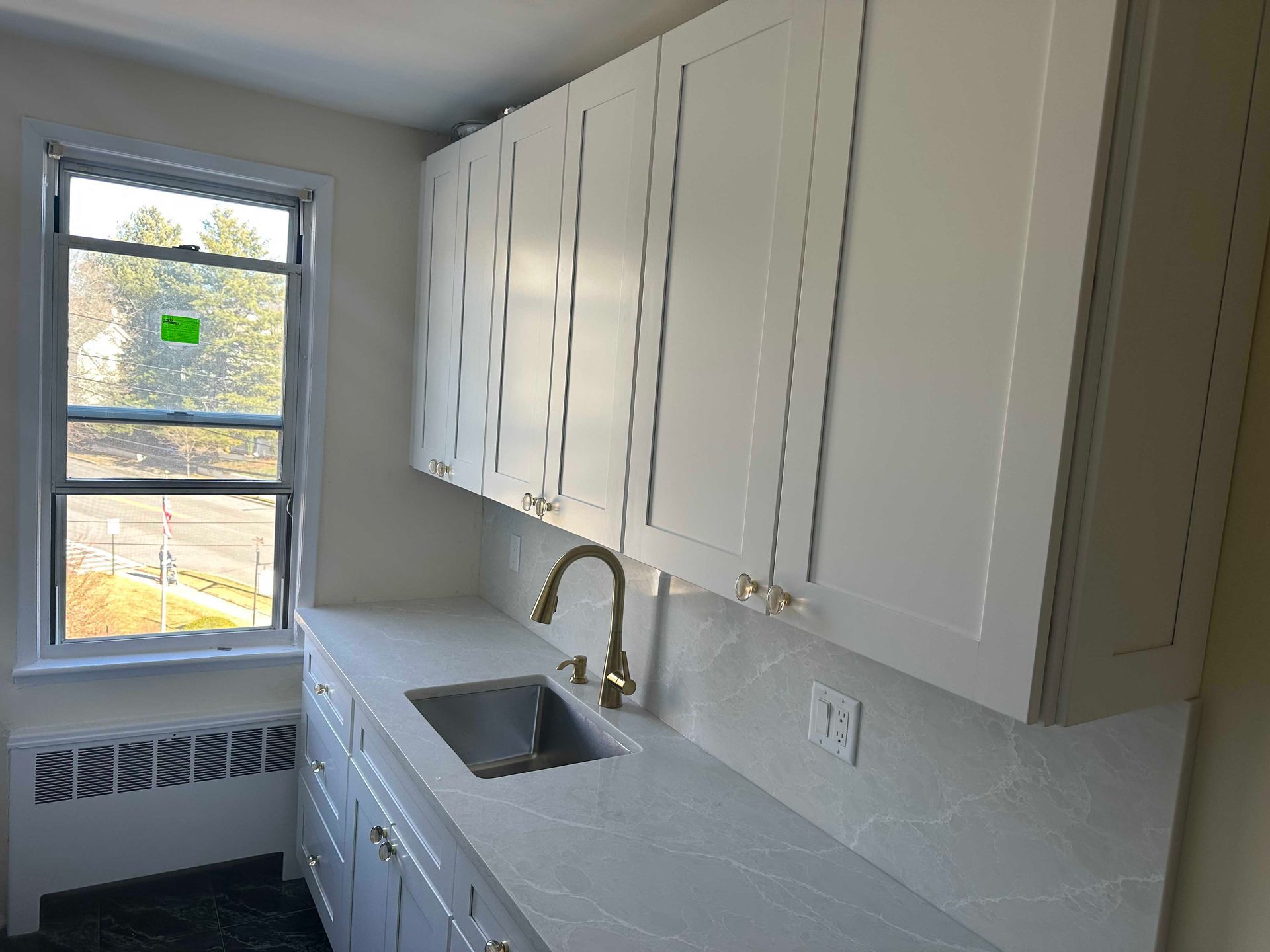 White kitchen cabinets, countertop, and sink by a window. Gold faucet and hardware.