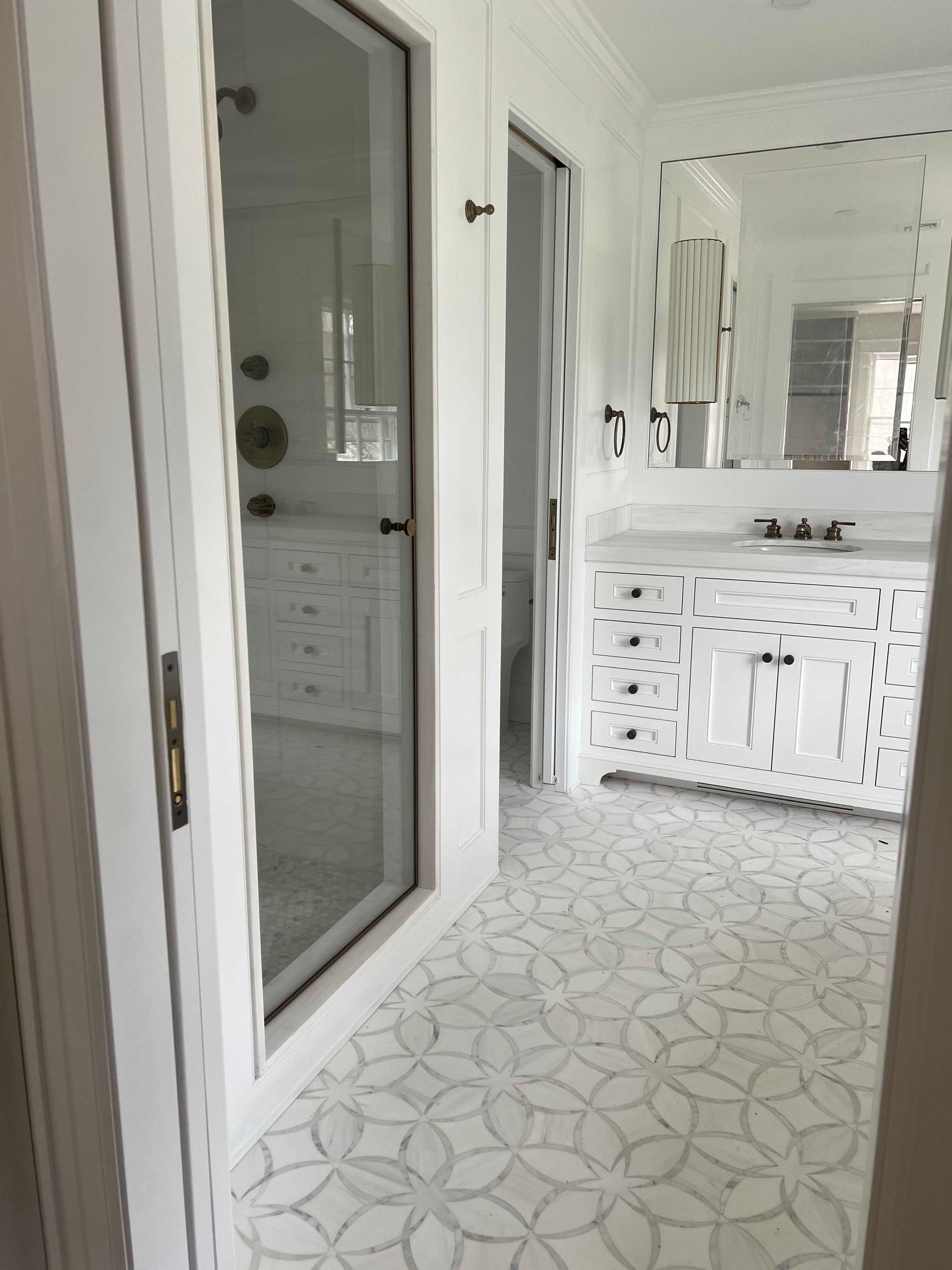 Bathroom with white cabinetry, patterned tile floor, and a glass-enclosed shower.
