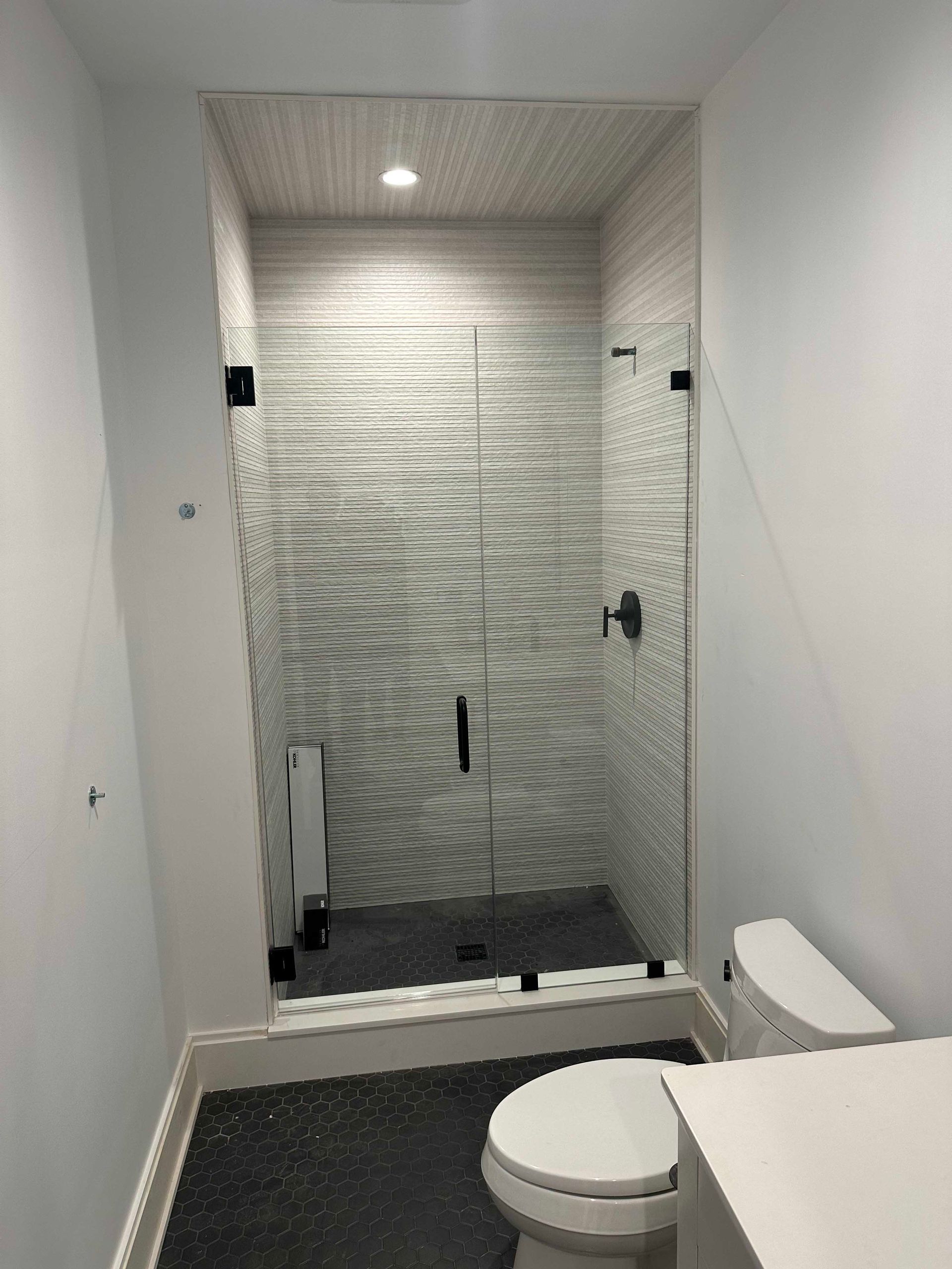 Small bathroom with glass shower door, black fixtures, and white walls.
