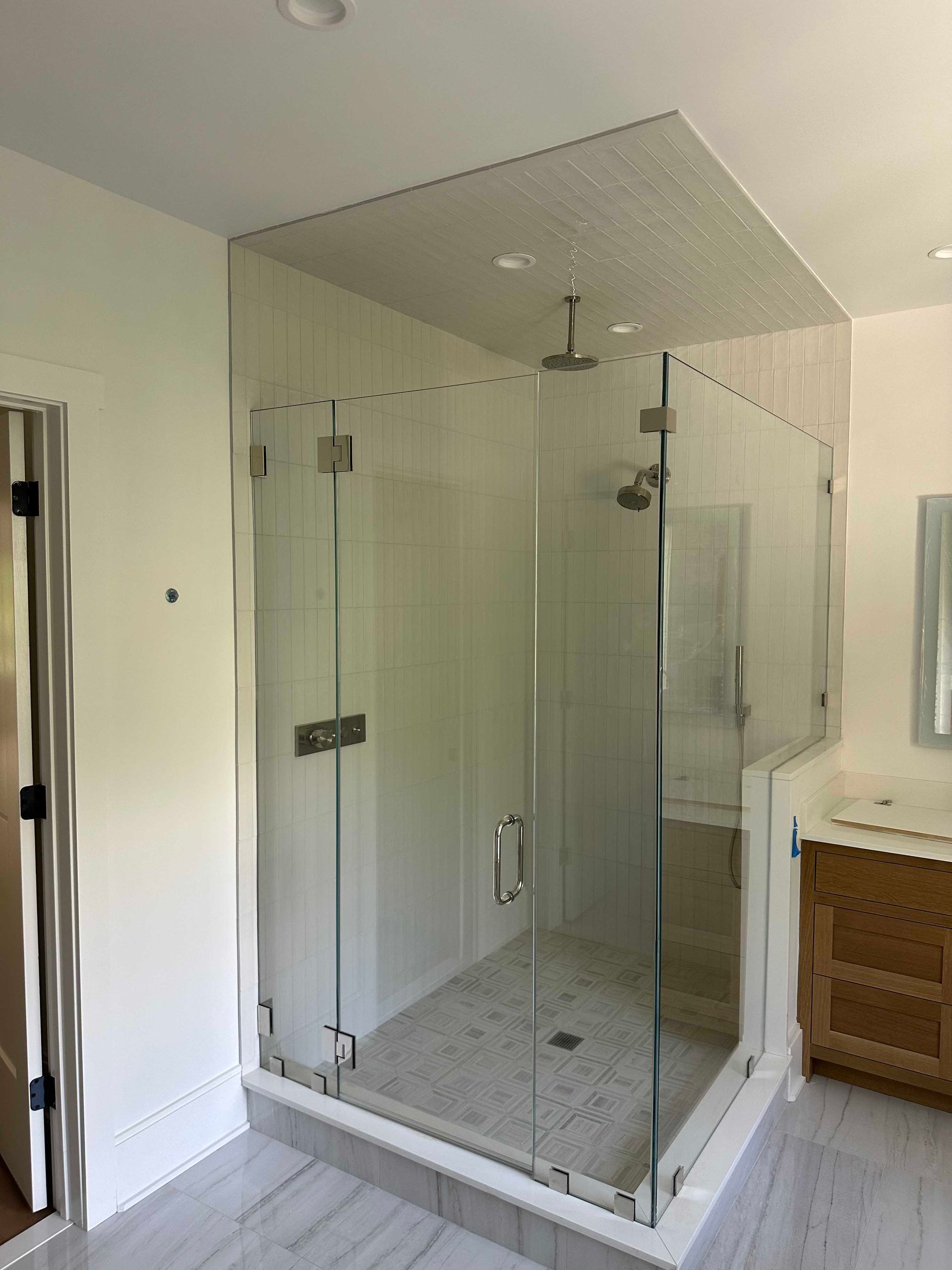 Glass-enclosed shower in a bathroom with light-colored tile and wooden vanity.