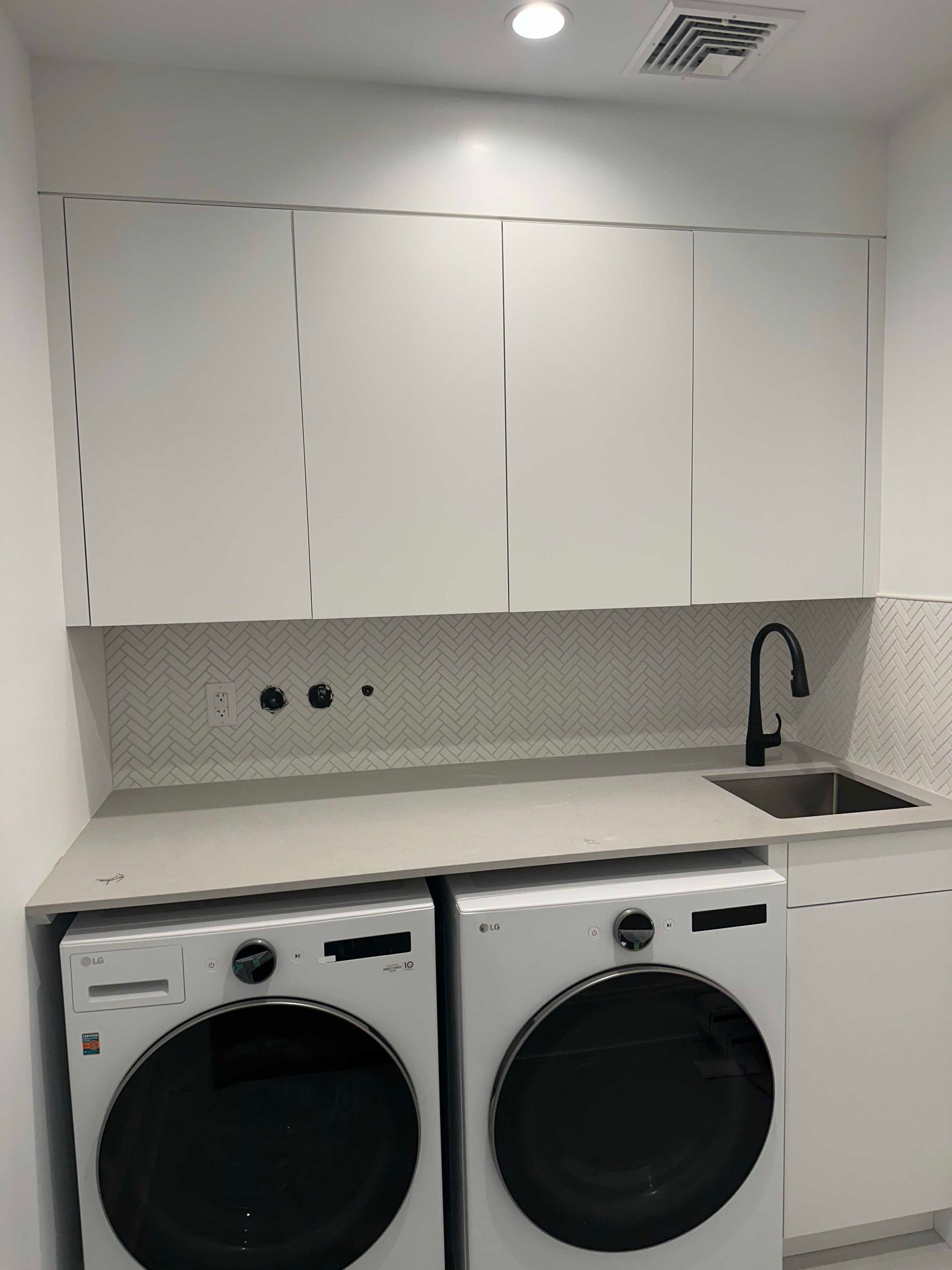 Laundry room with white cabinets, washer and dryer, countertop, sink, and backsplash.