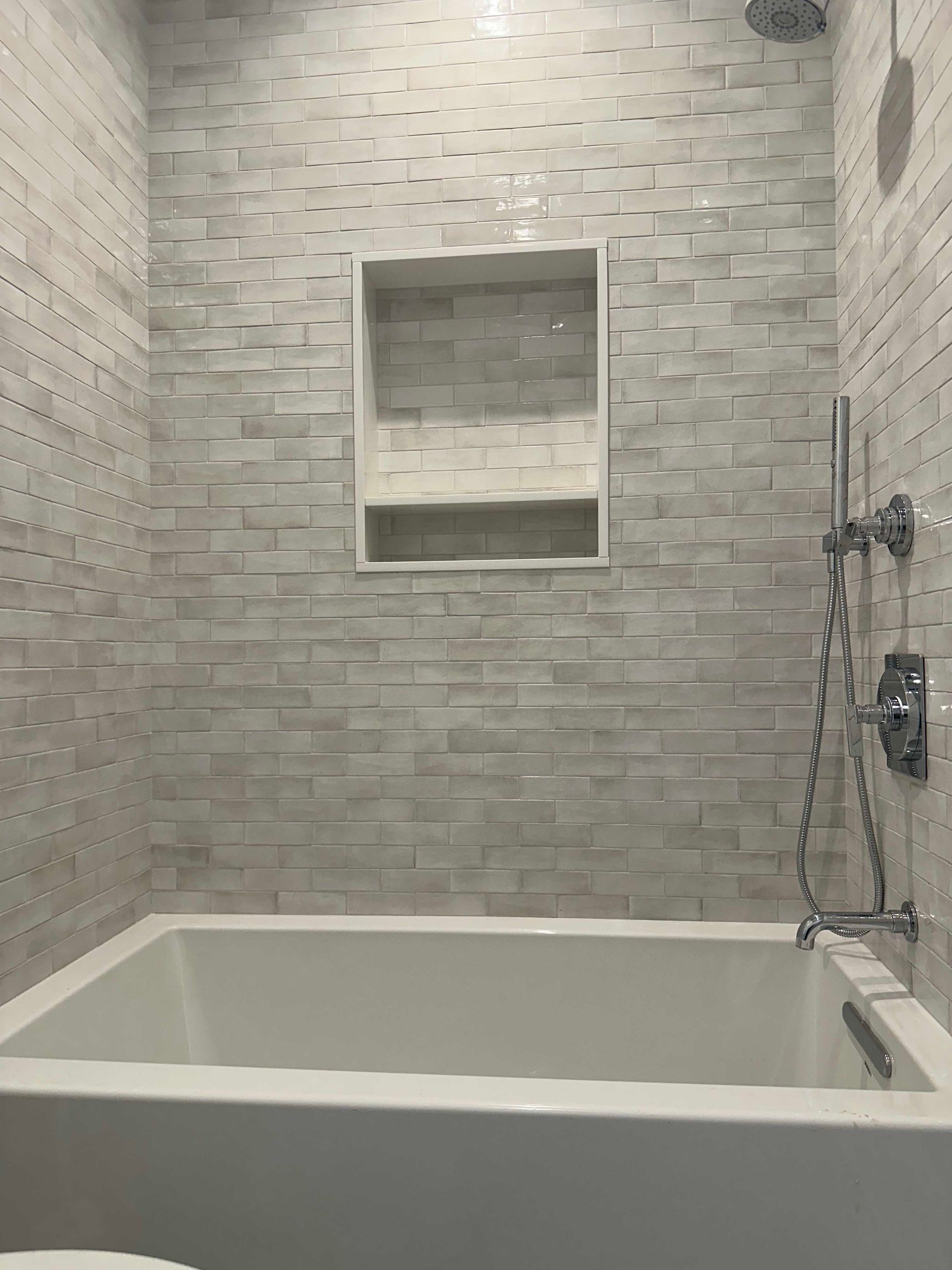 Bathroom with white rectangular textured wall tiles, a recessed shelf, and a white bathtub.