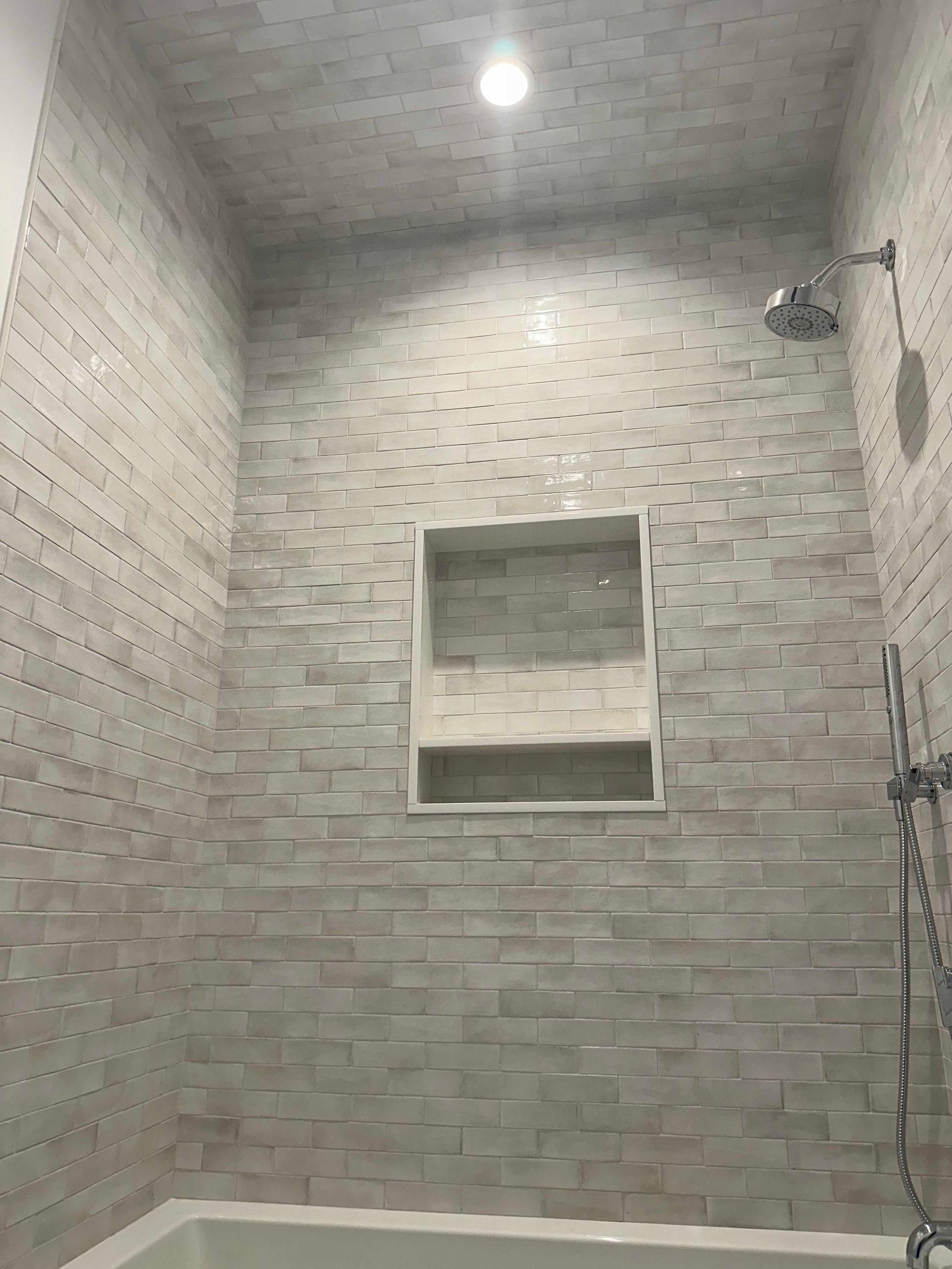 Shower stall with gray textured tile, recessed shelf, and chrome fixtures.