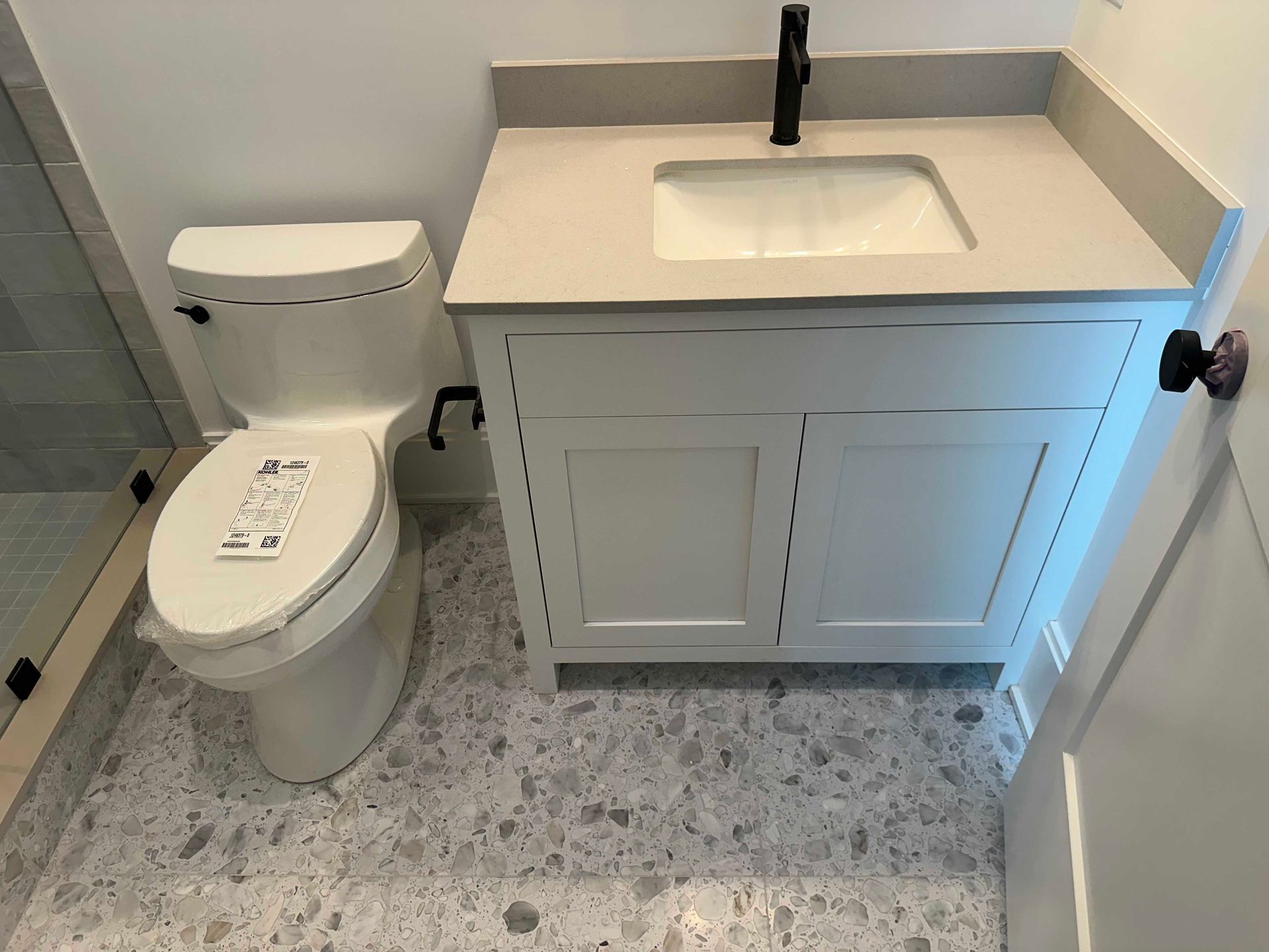 Bathroom with white toilet, vanity, black faucet, and patterned flooring.