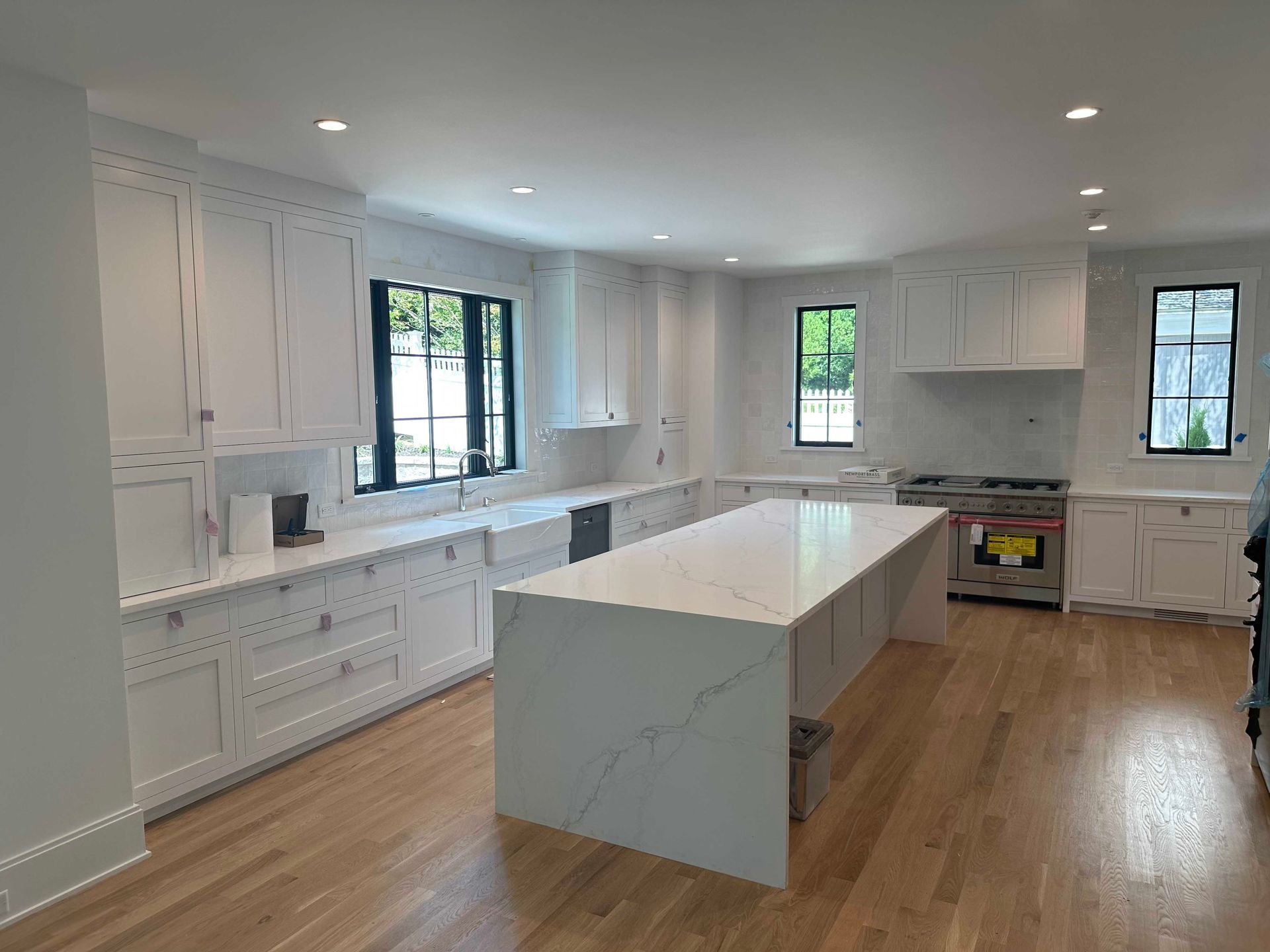 White kitchen with large island, wood floors, white cabinets, and dark-framed windows.