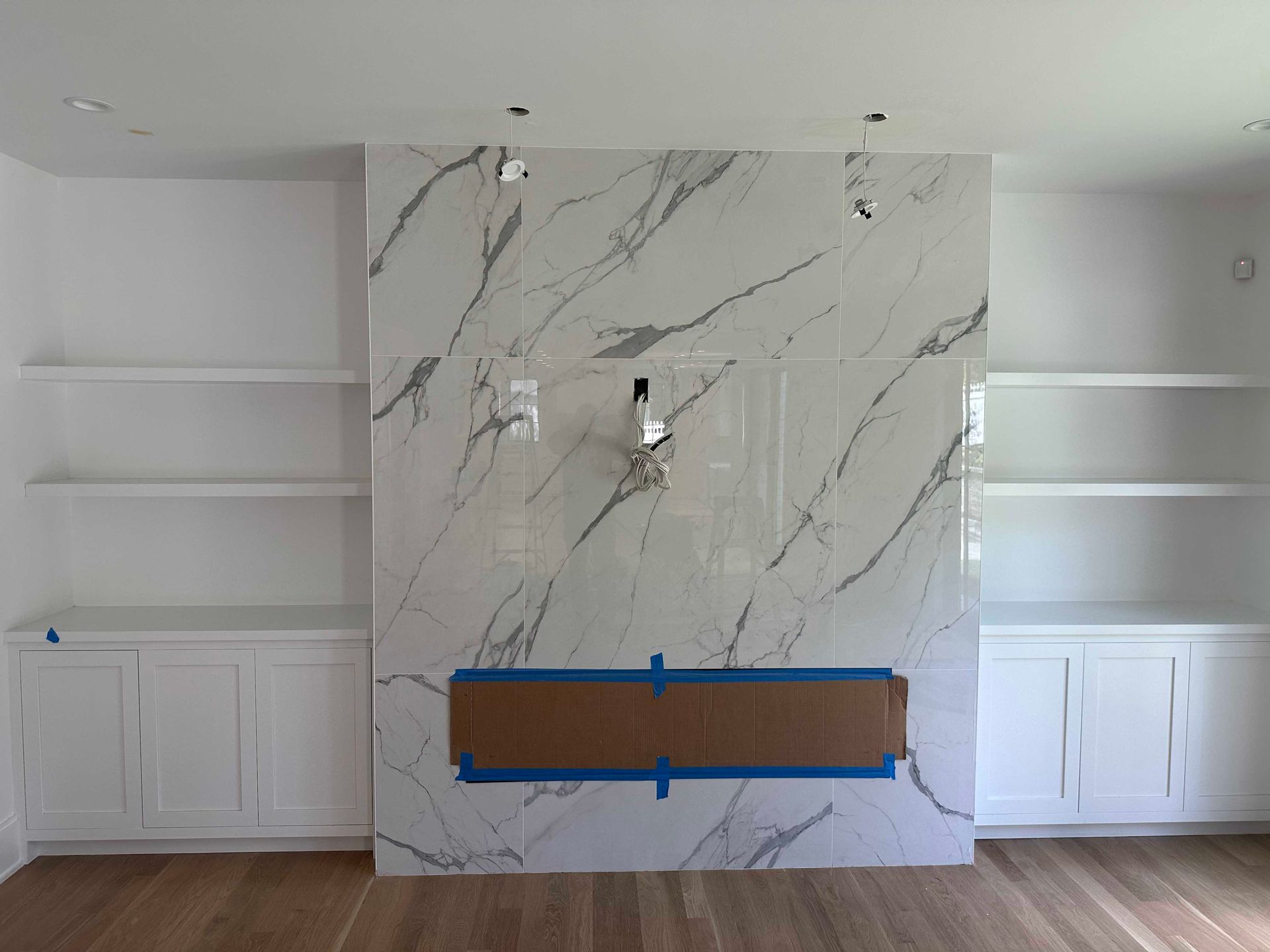 Fireplace wall with marble-look tile, built-in white bookshelves and cabinets, brown floor, and a covered fireplace opening.
