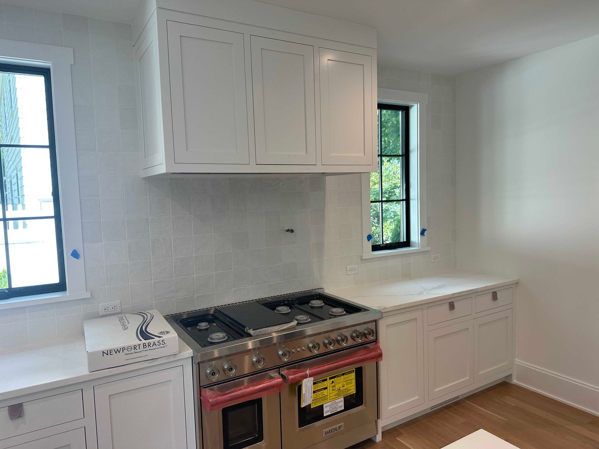 White kitchen with stainless steel range, white cabinets, and black-framed windows.