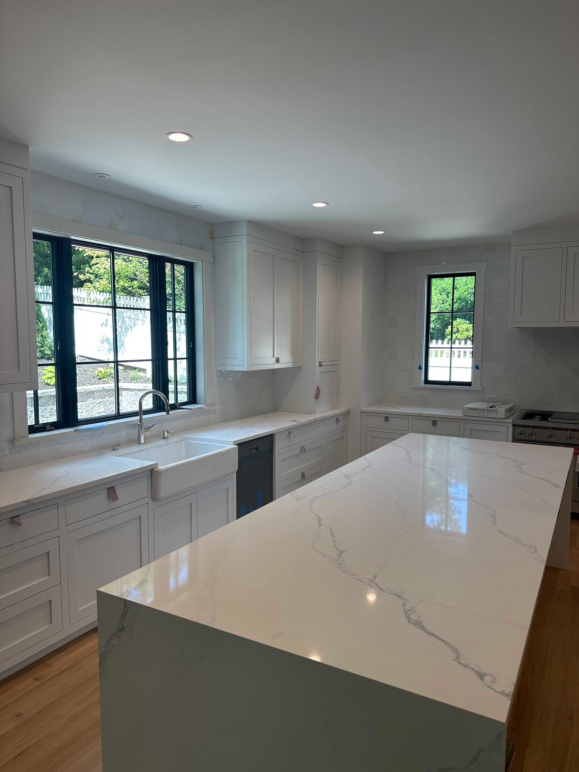 White kitchen with large island and black-framed windows; quartz countertops and white cabinetry.
