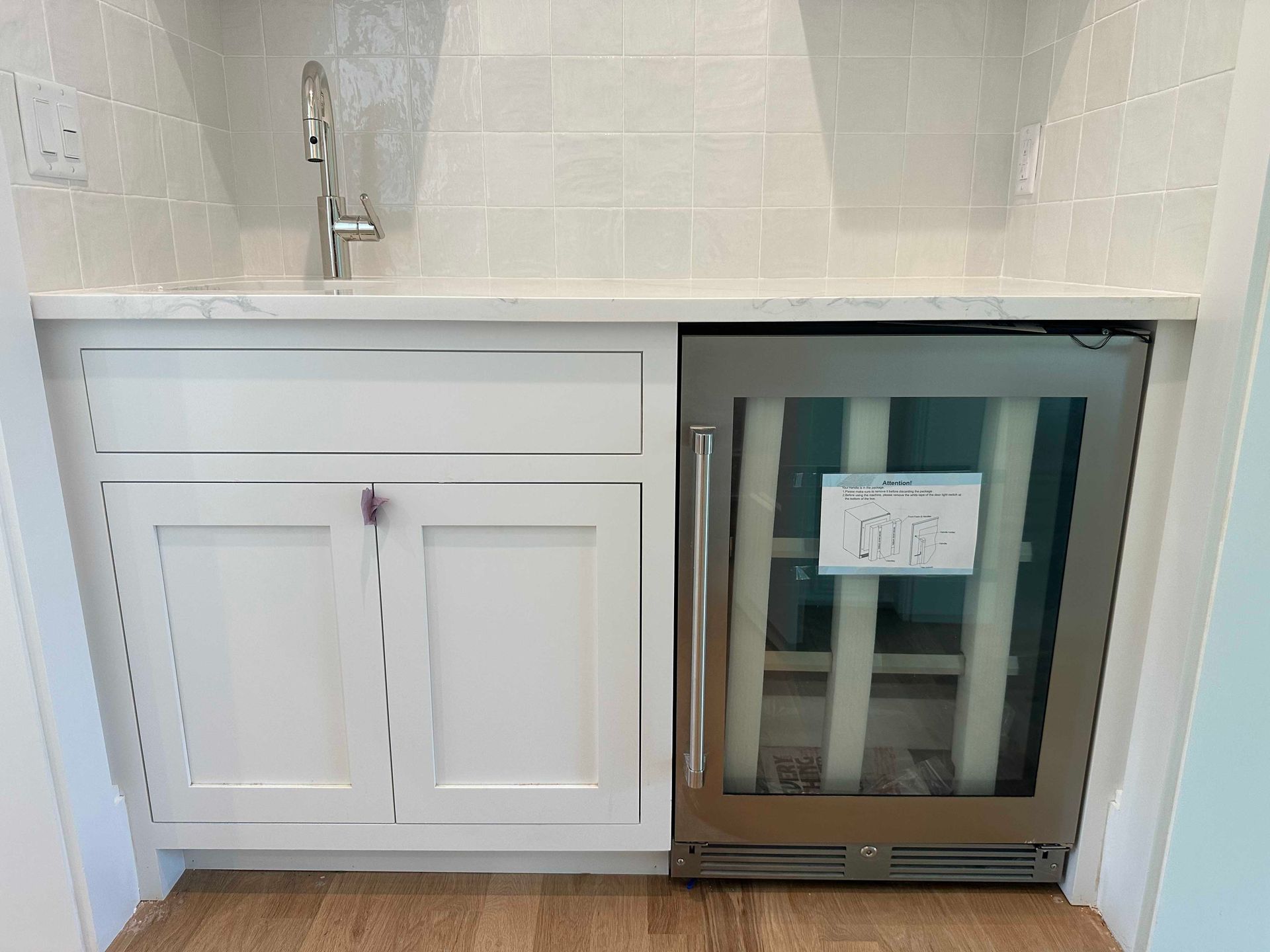White cabinets and a stainless steel beverage cooler under a sink, set against tiled backsplash.