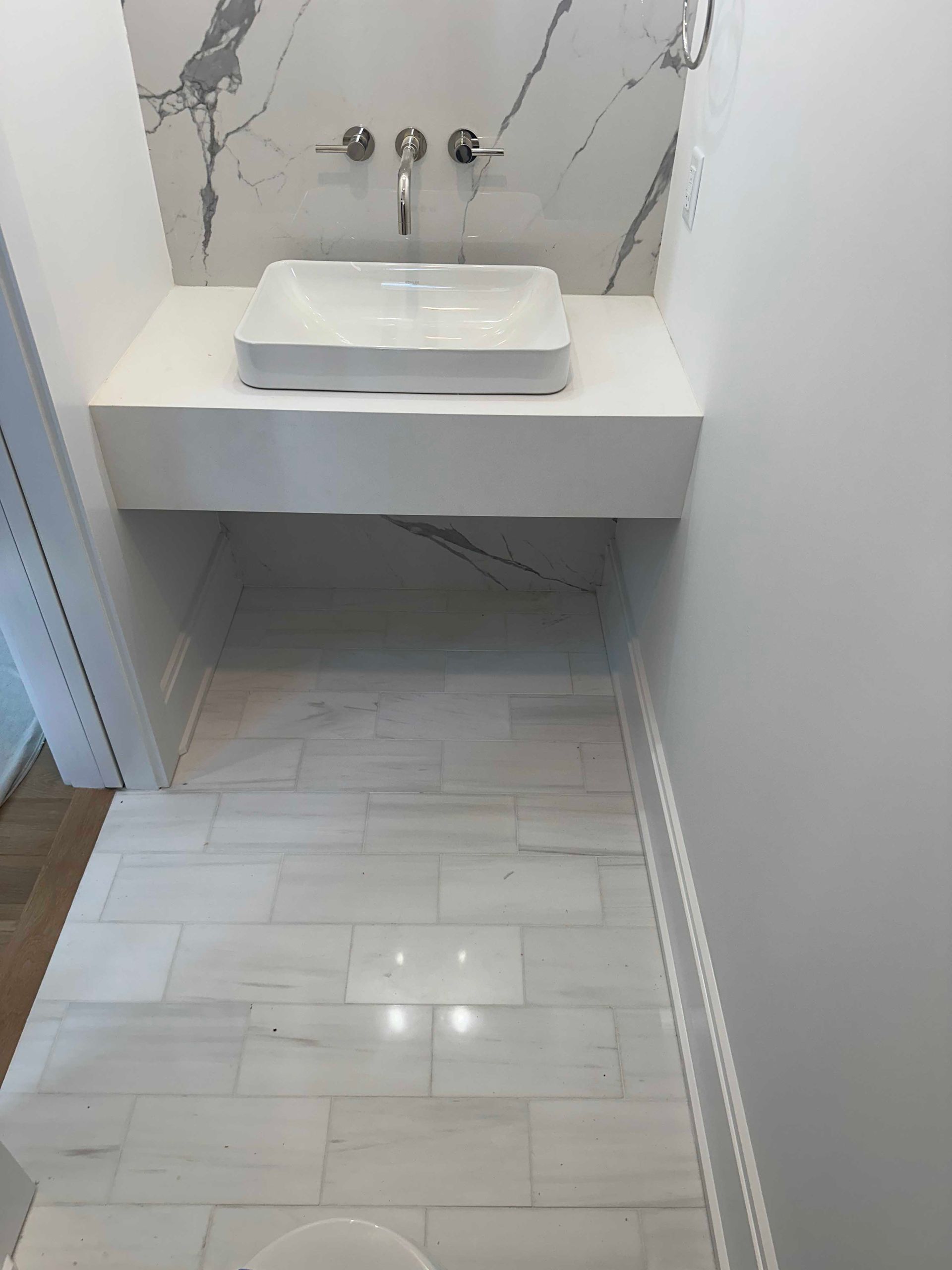 Modern bathroom with white floating sink and marble-look wall and floor tiles.
