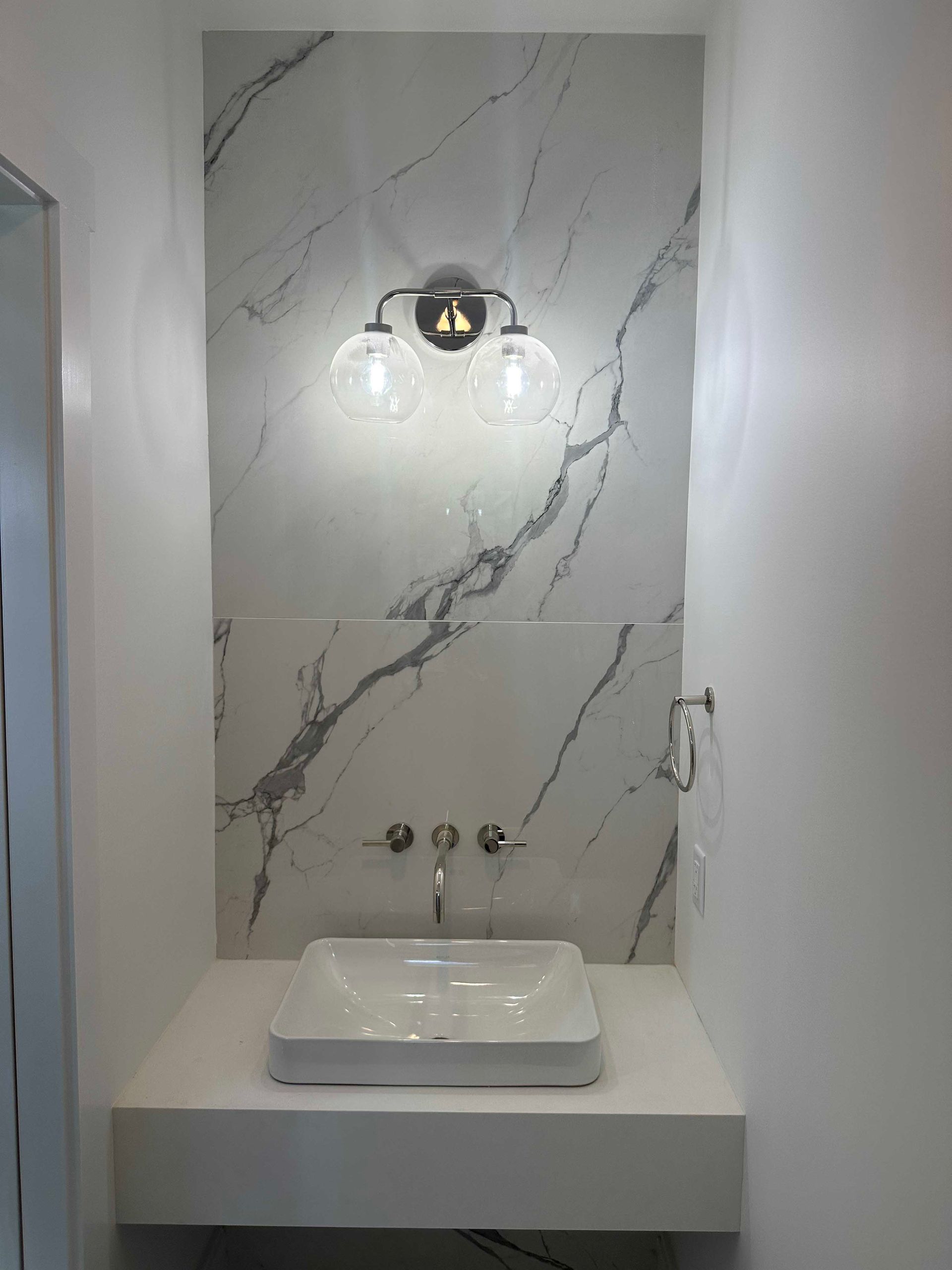 Bathroom with white marble accent wall, floating sink, chrome fixtures, and a dual-light fixture.