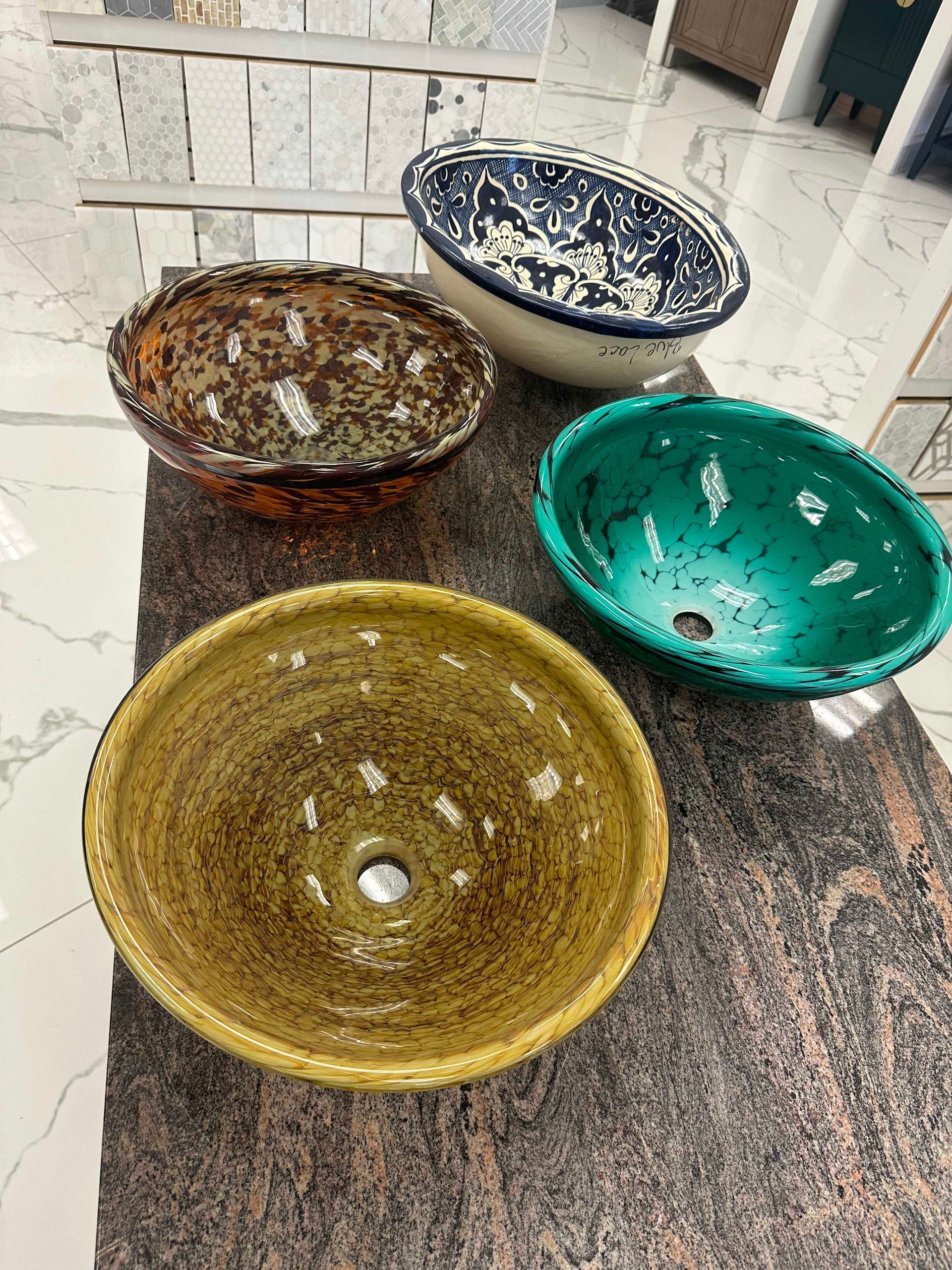 Four colorful ceramic vessel sinks on a textured, brown surface.