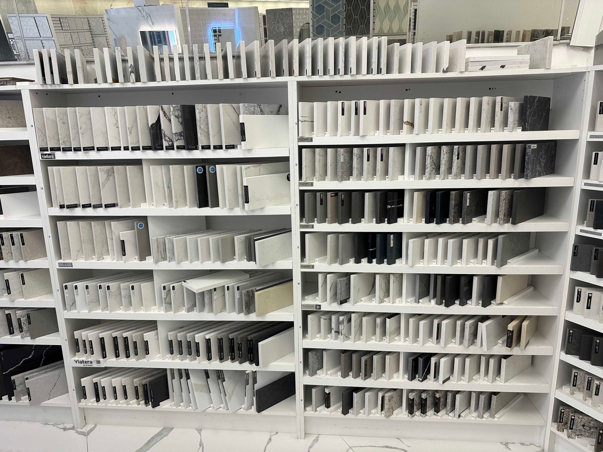 Shelves filled with various stone samples, primarily gray and white, in a showroom.