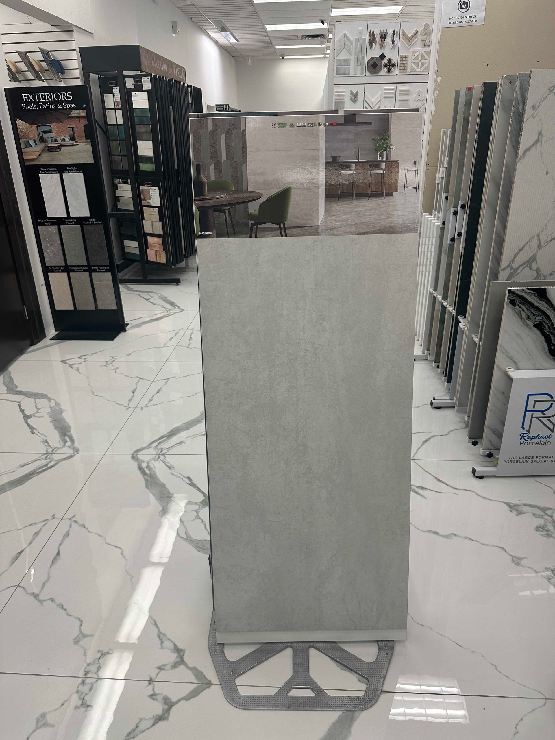 Large gray tile on display in a showroom, surrounded by other tile samples and displays.