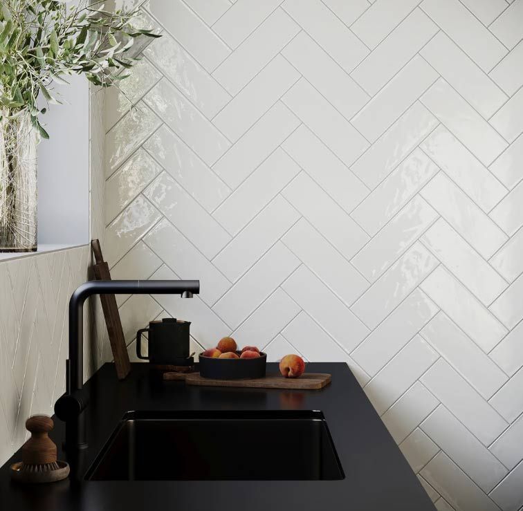 White herringbone tile backsplash above a black kitchen countertop and sink.
