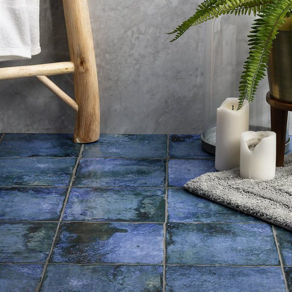 Blue tiled bathroom floor with a wooden ladder, candles, and a fern.