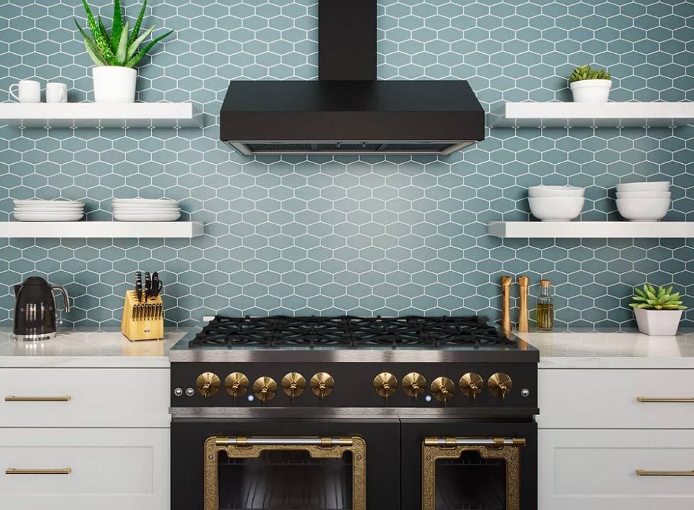 Kitchen with blue mosaic tile backsplash, black range hood, stove, and white cabinets.