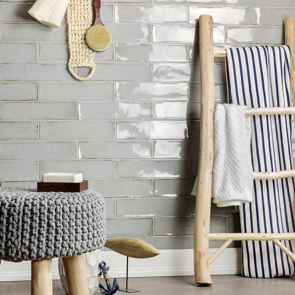Bathroom with gray tiled wall, wooden ladder with towels, and a gray knitted stool.