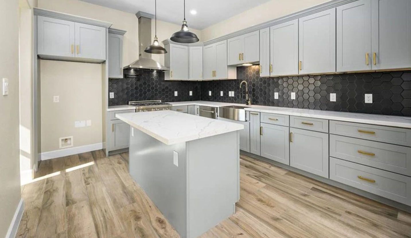 Modern kitchen with light gray cabinets, white countertop island, black hexagon backsplash, and light wood floors.