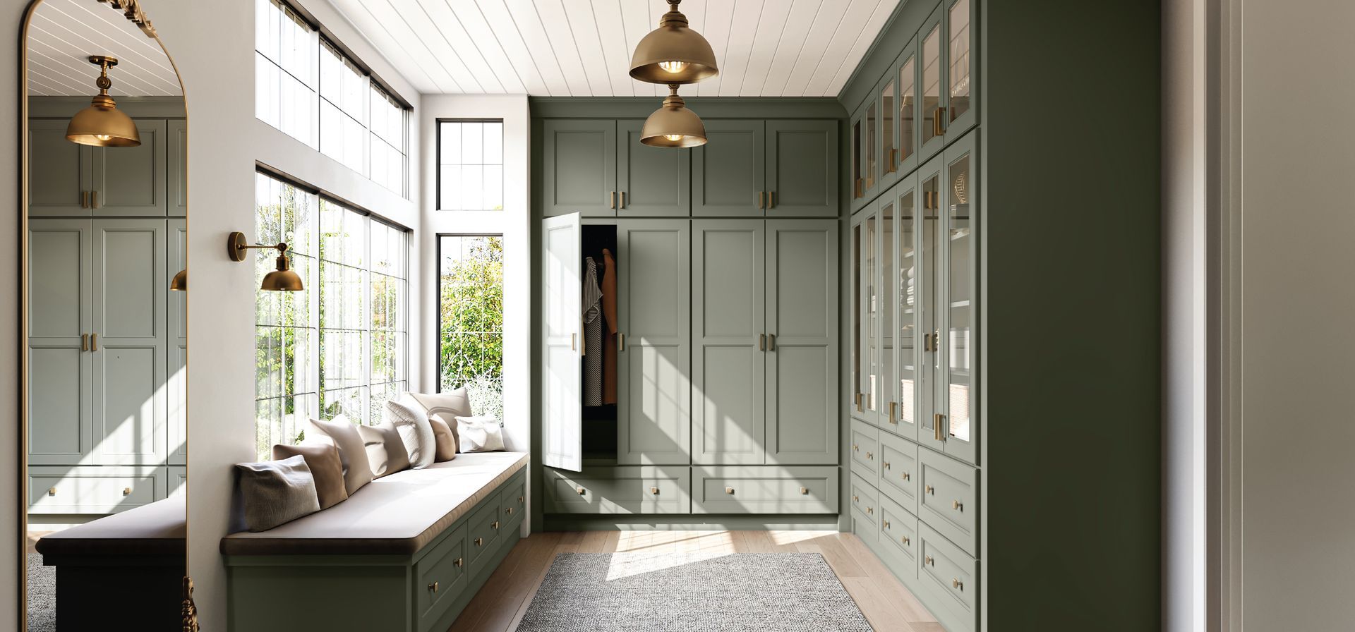 A walk-in closet with green cabinets, a window seat, and a large mirror.
