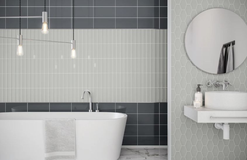 Modern bathroom with a white bathtub, round mirror, and gray tiled walls.