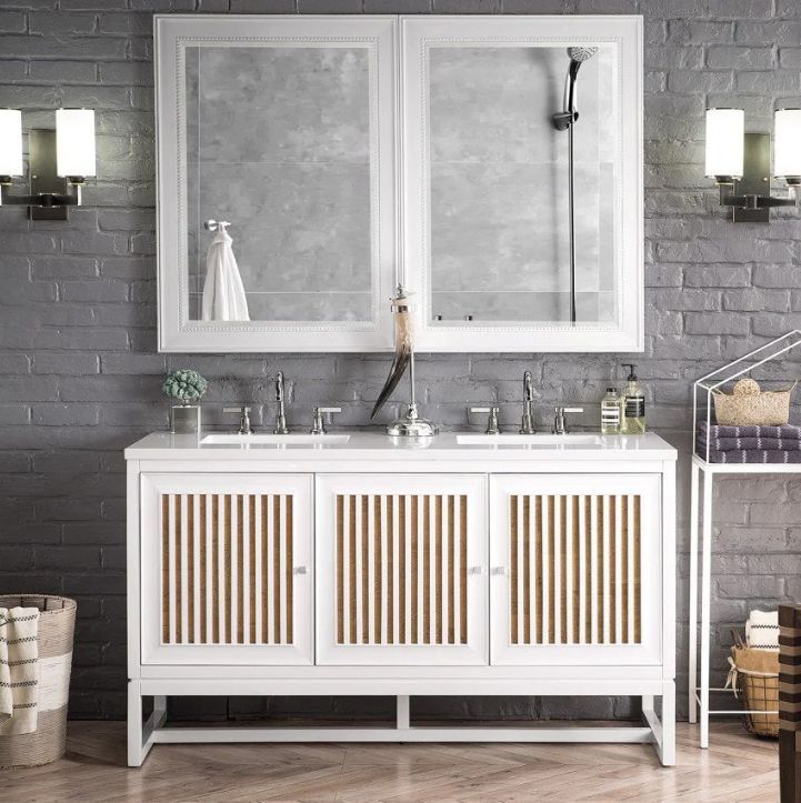 White bathroom vanity with two sinks, two mirrors, and wall sconces against a gray brick wall.