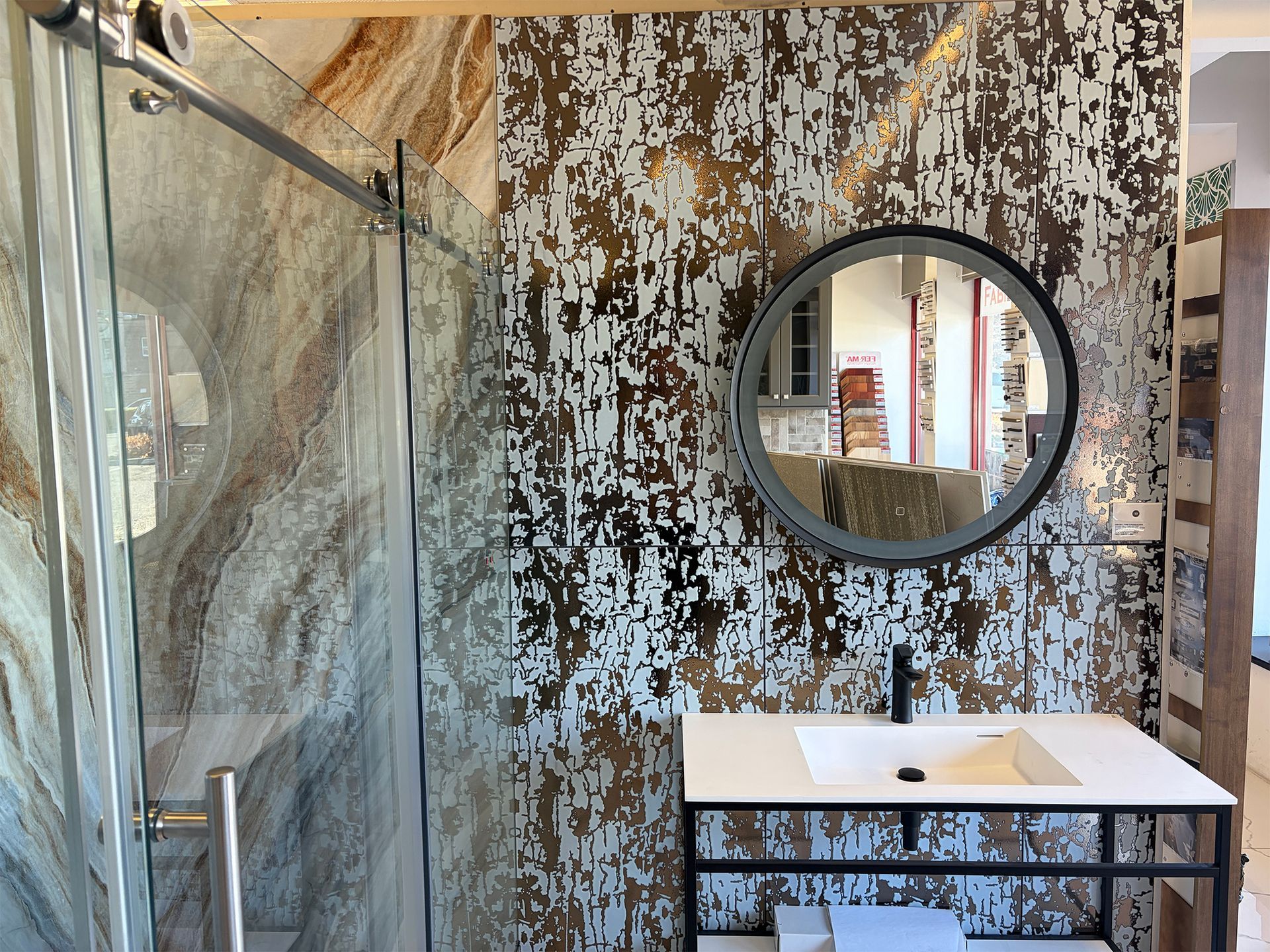 Bathroom with glass shower door, patterned accent wall, round mirror, and white sink.