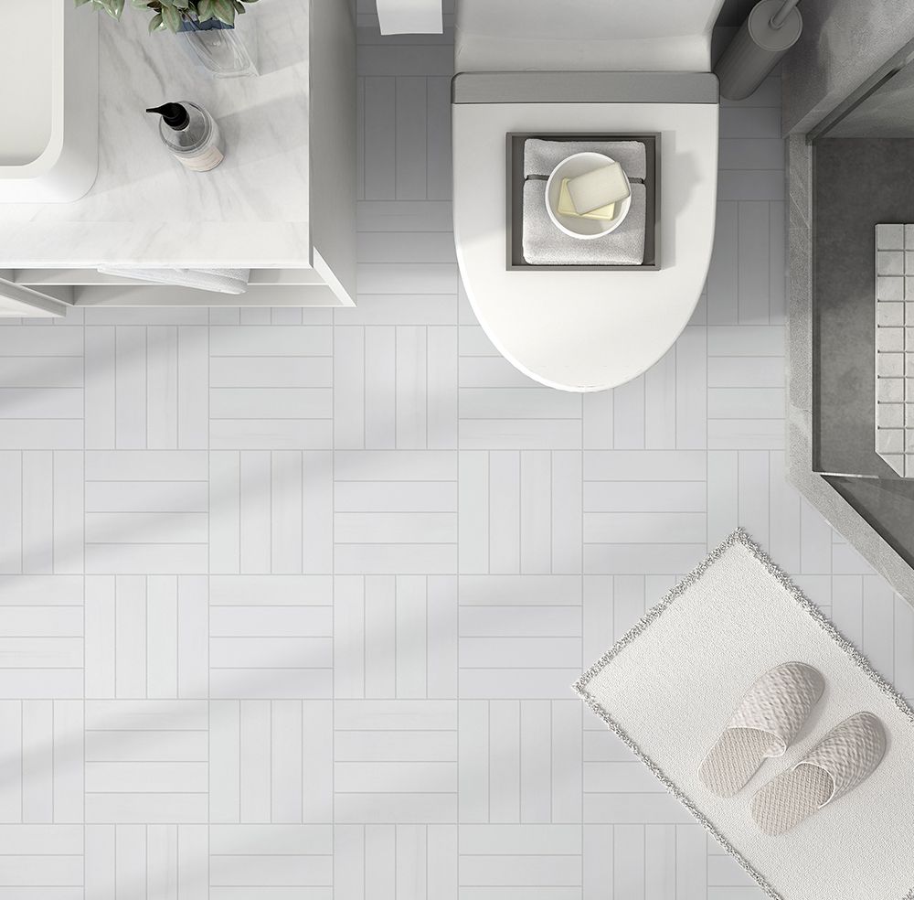 Overhead view of a white bathroom with a toilet, sink, and tiled floor. A mat with slippers sits on the floor.