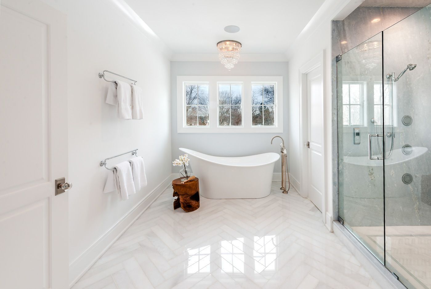 Spacious white bathroom with freestanding tub, glass shower, and marble floors.