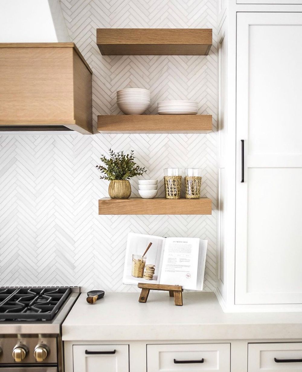 Kitchen with wooden shelves holding bowls and plants against a patterned backsplash, beside white cabinets and stove.