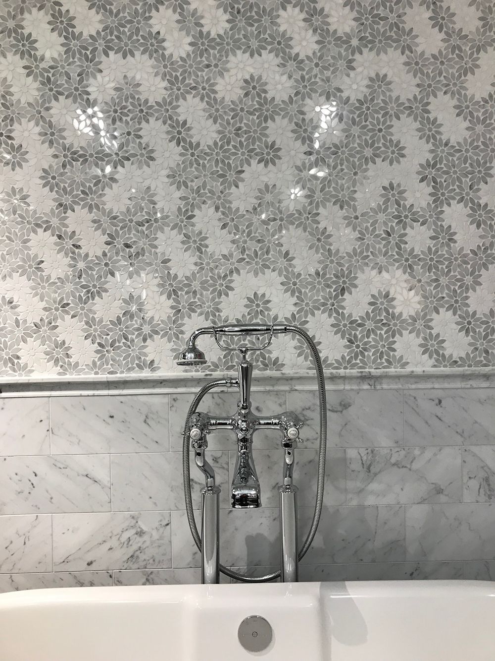 Tub with ornate chrome fixtures, white tile backsplash with floral pattern.