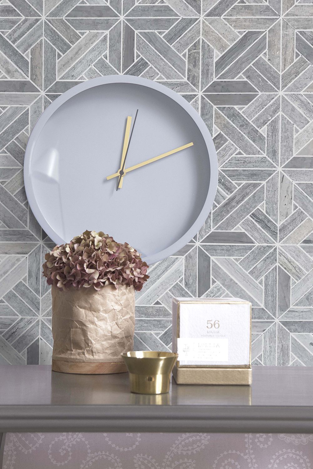 Clock, vase with flowers, and candle on a gray surface against patterned gray and white tile.