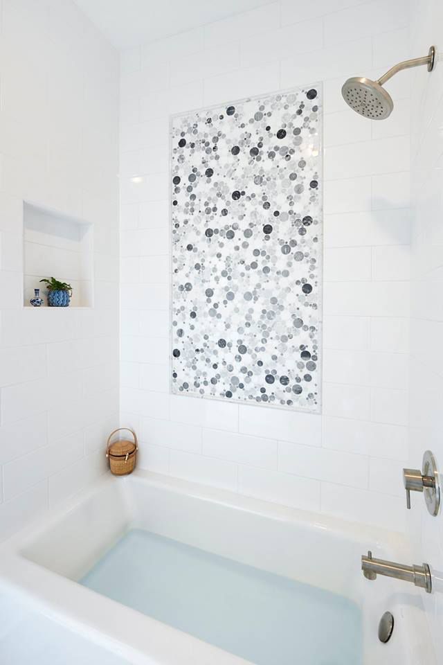 White bathroom with tub, showerhead, and decorative tiled accent.