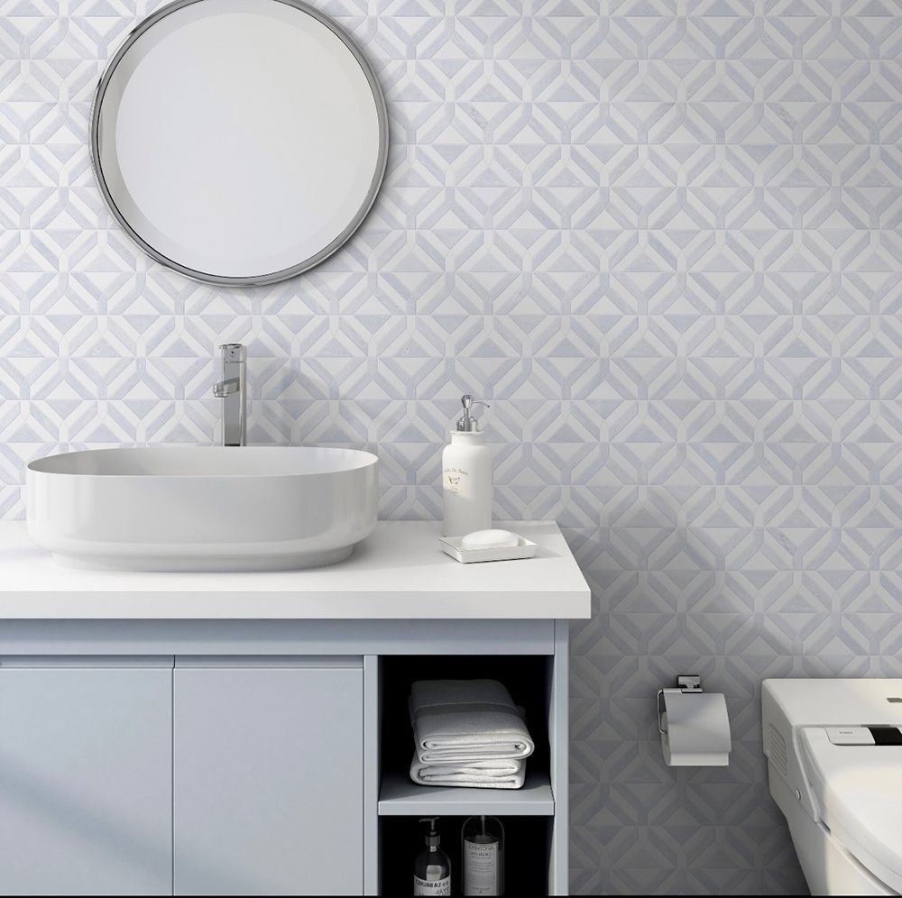 Bathroom with white sink, blue cabinet, round mirror, and patterned tile wall.