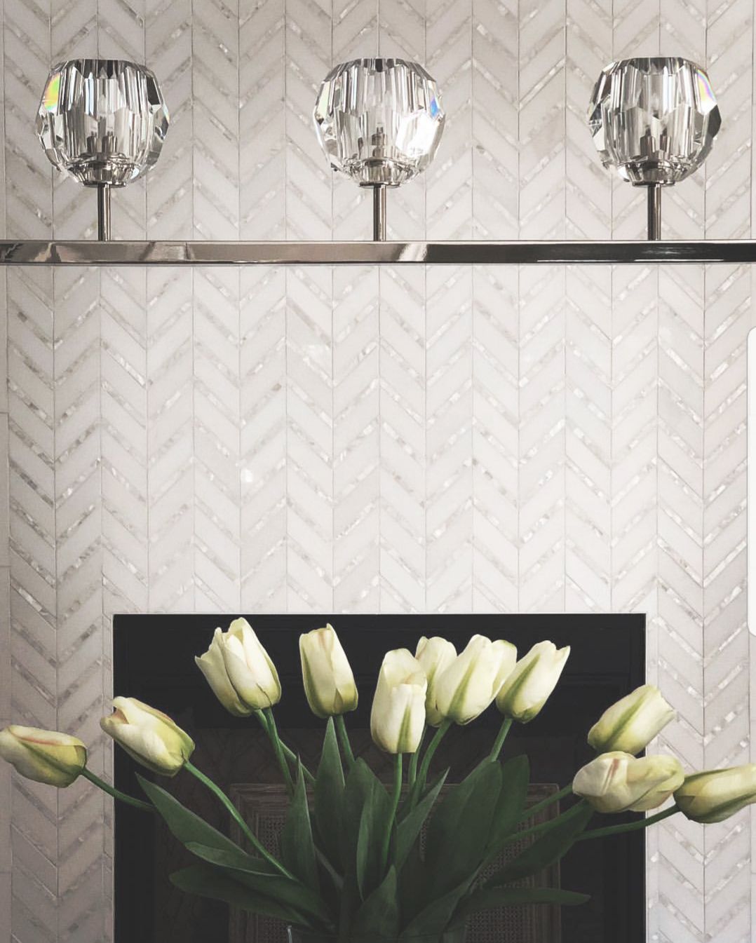 Three crystal sconces above a fireplace with white chevron tile, and a bouquet of white tulips.