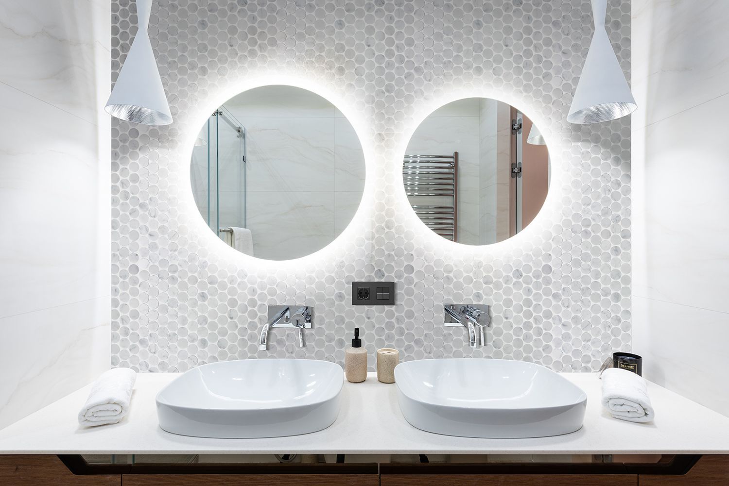 Bathroom with two sinks, round mirrors with lights, and white honeycomb tile backsplash.
