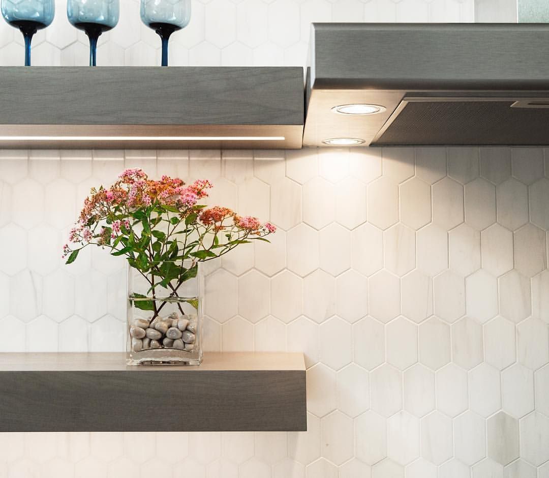 Kitchen with gray shelves, flower vase, white tiled backsplash, and recessed lighting.