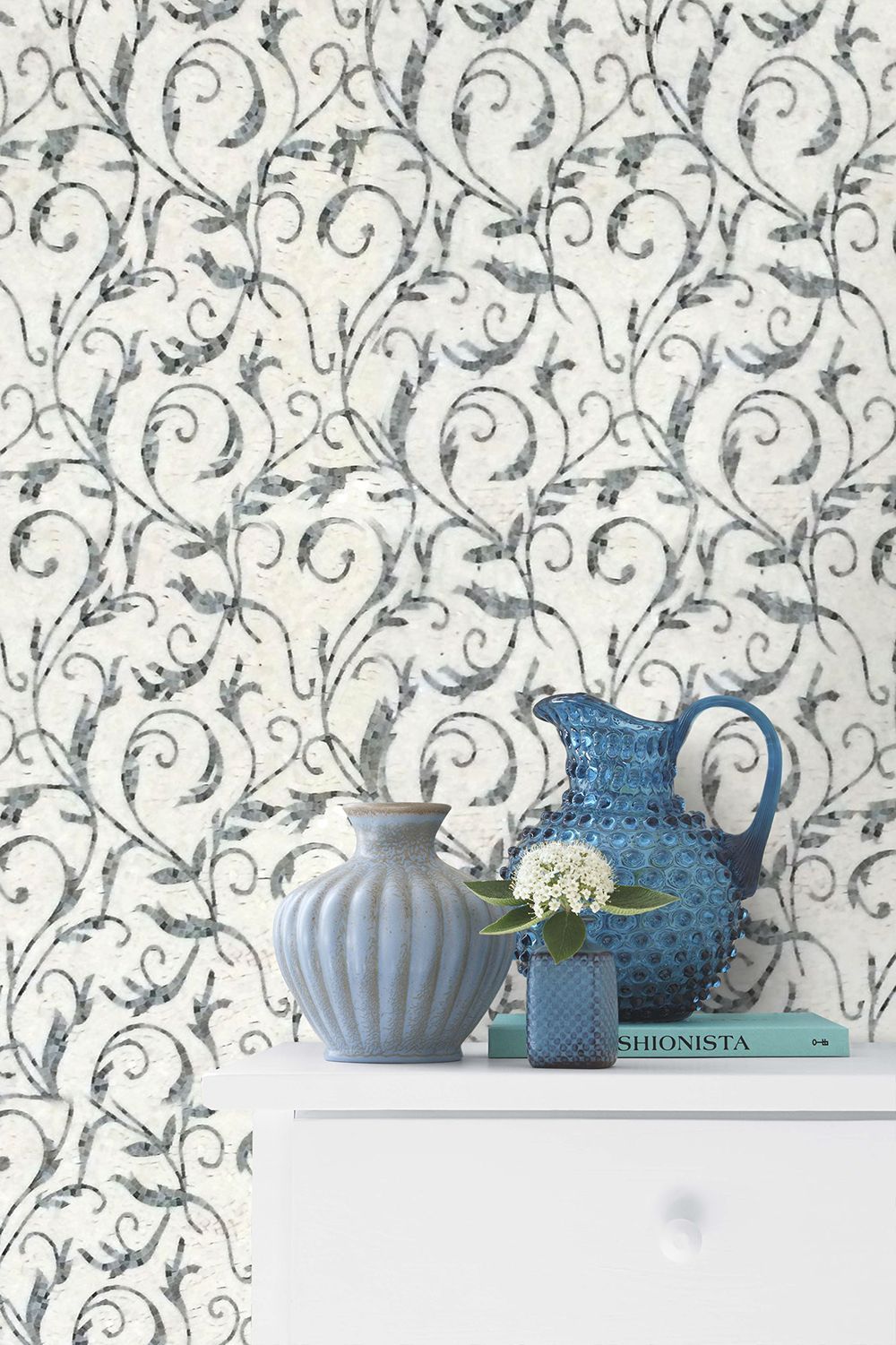 White and blue wallpaper with floral pattern. White dresser with blue vases and book.