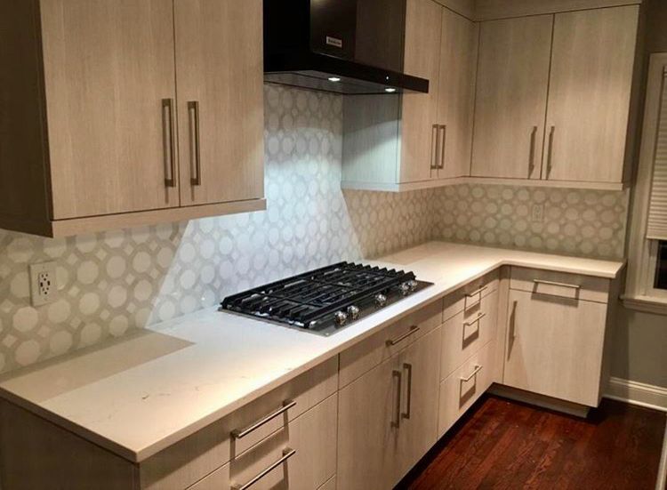 Modern kitchen with light wood cabinets, white countertops, and patterned backsplash.
