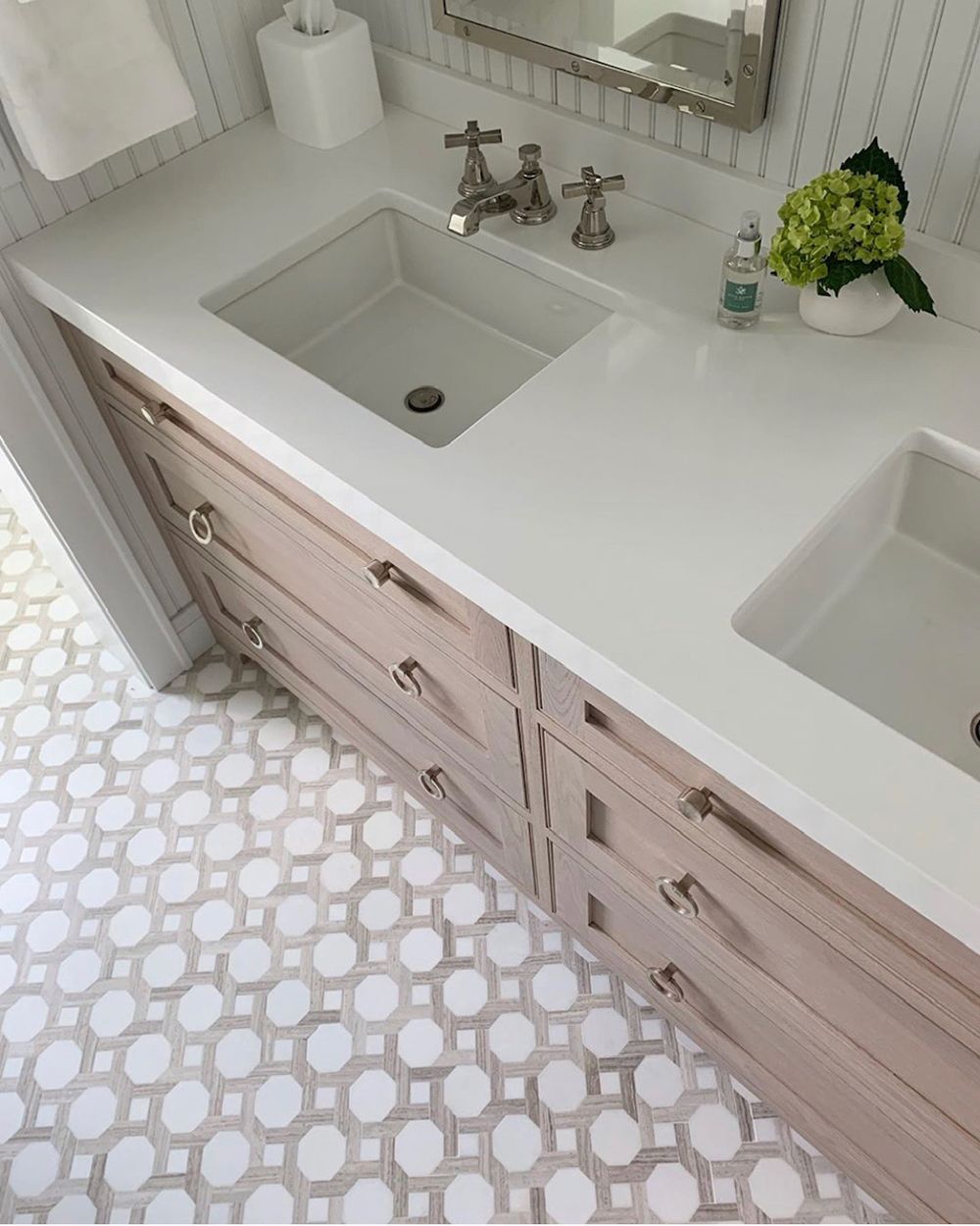 Bathroom with white countertop, two sinks, light wood vanity, and patterned floor tiles.