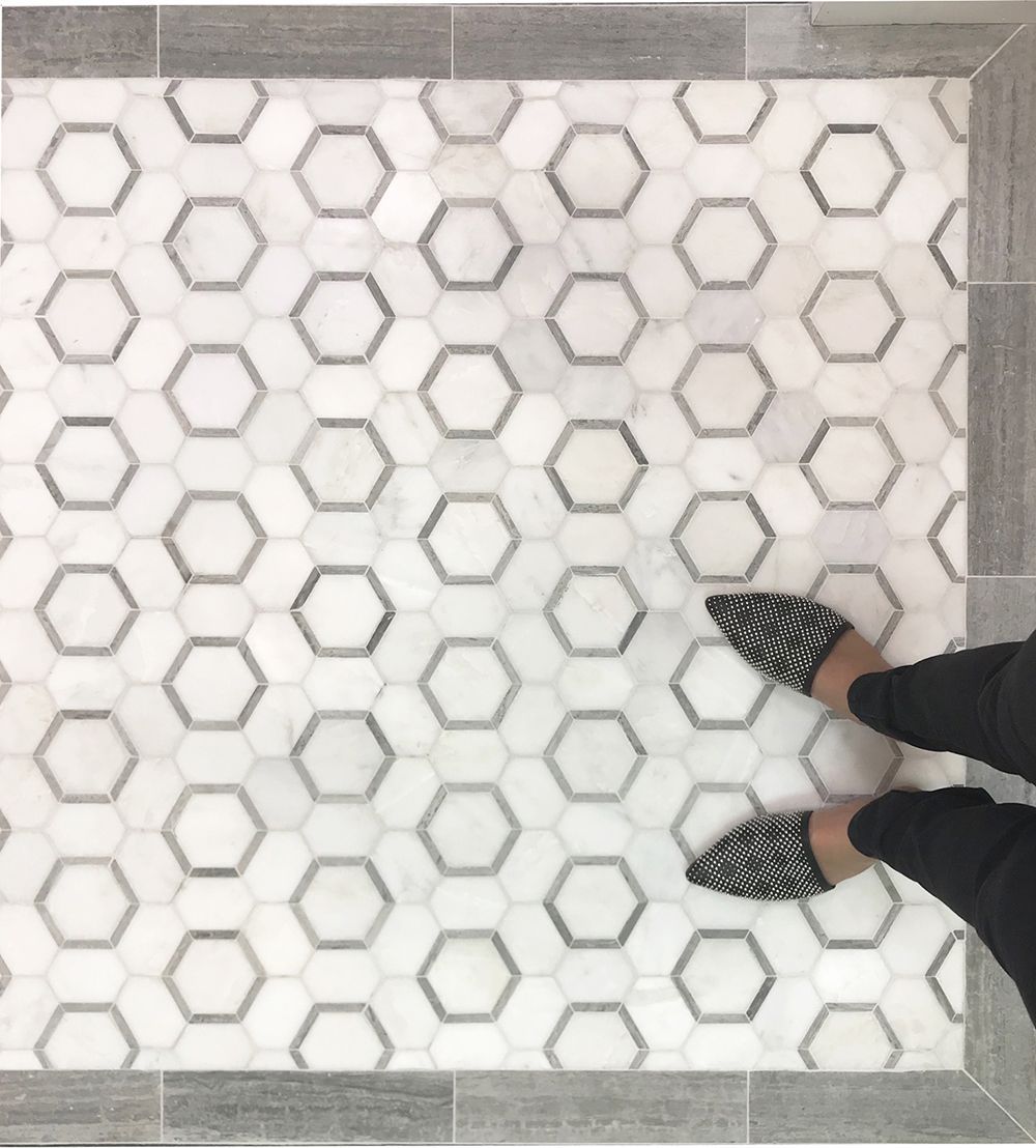 Feet wearing patterned shoes on hexagon tile floor. Gray border surrounds tiles.